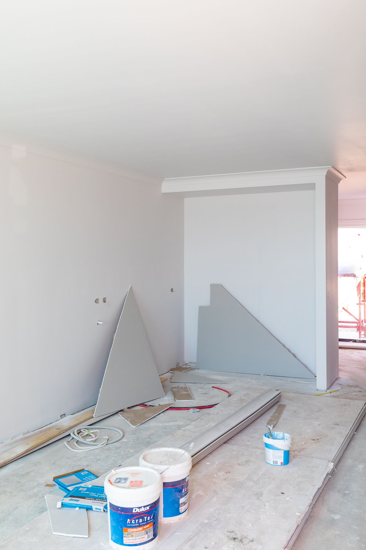 Unfinished living room under construction with plasterboard offcuts, paint tins and building materials on a dusty floor.