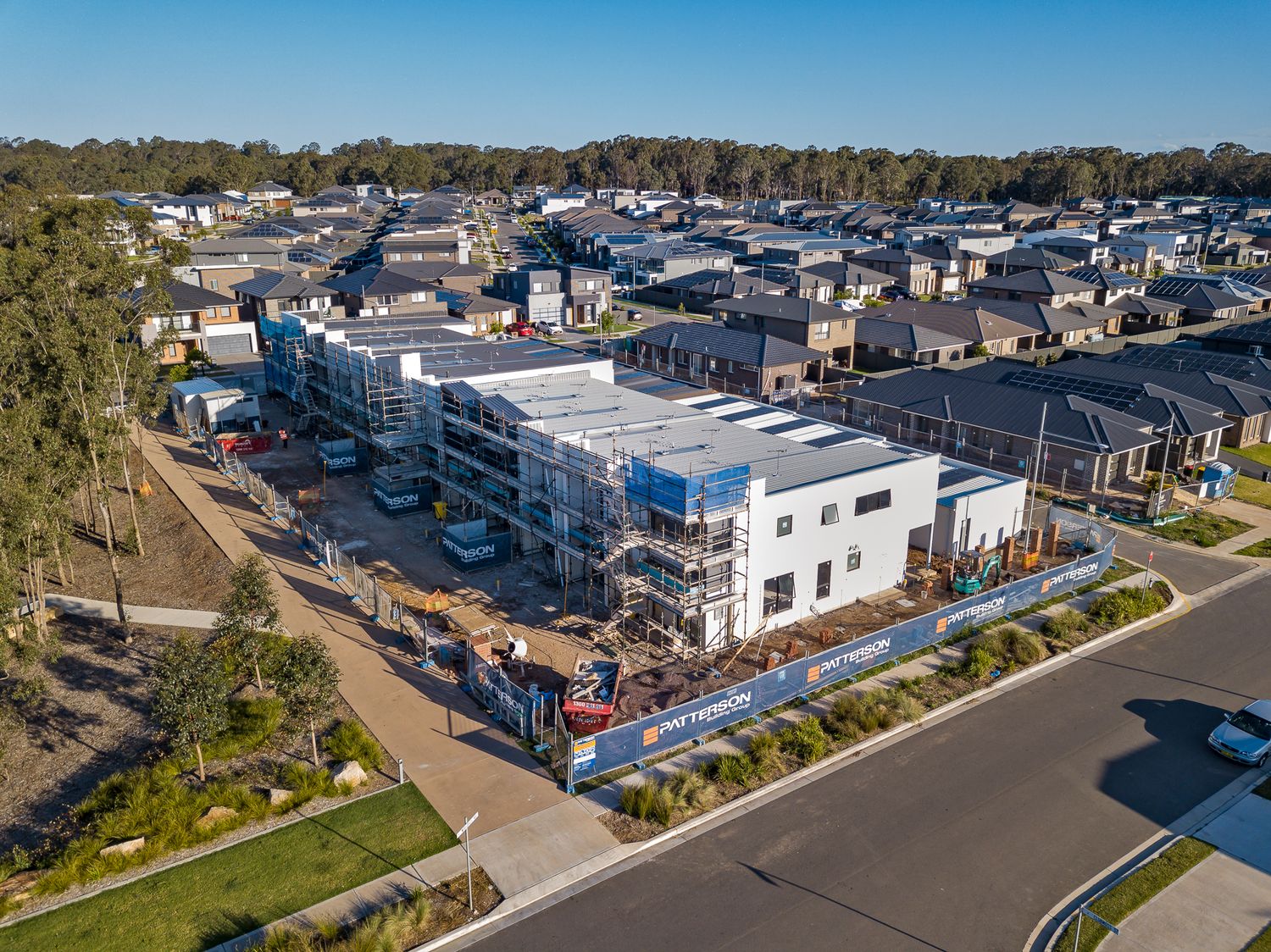 Aerial view of a multi-storey townhouse complex under construction with scaffolding, beside a suburban street and homes.