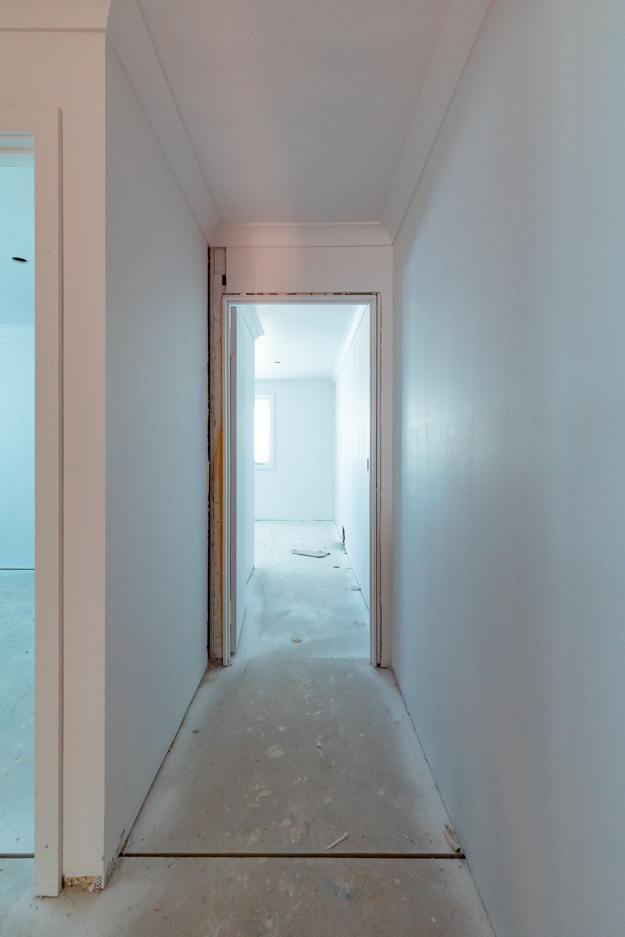 Narrow hallway in a new home under construction with freshly plastered walls and an open doorway leading to another room.