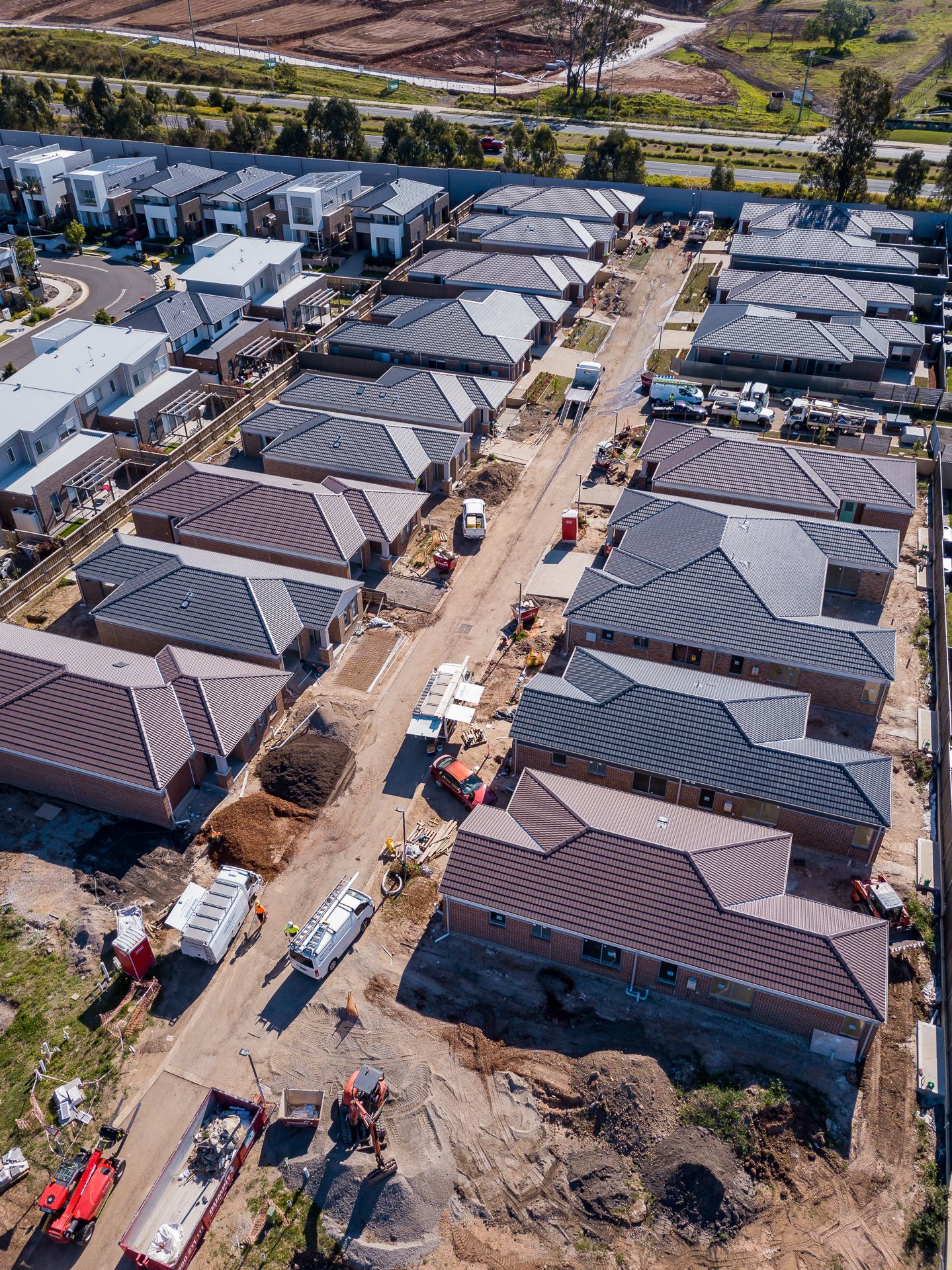 Aerial view of a residential construction site with new brick homes, grey tiled roofs, and dirt streets under development.