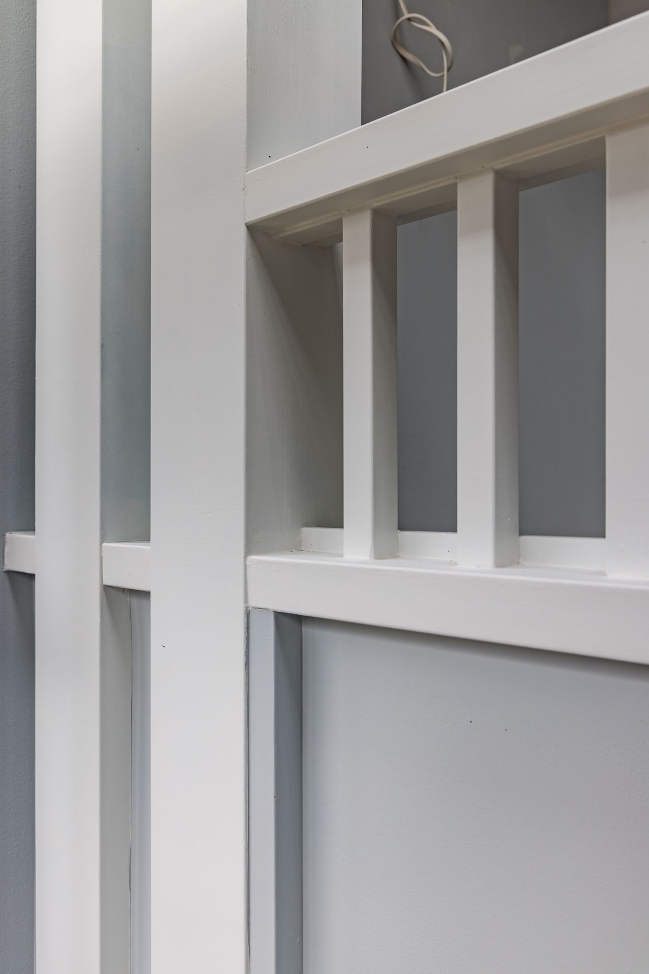 Close-up of white painted timber wall paneling and slatted balustrade detail against soft grey walls in a renovated interior.