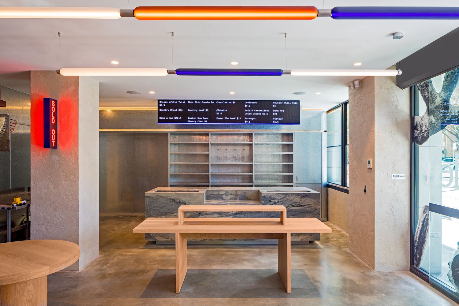 Modern cafe interior with colorful neon tube lights, a digital menu board, wooden tables and concrete counter shelving.