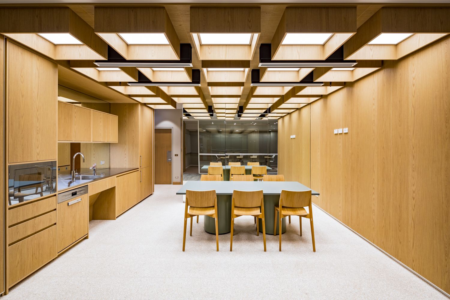 Bright timber-clad kitchen and dining area with a coffered wooden ceiling, built-in cabinetry and a long table with chairs.