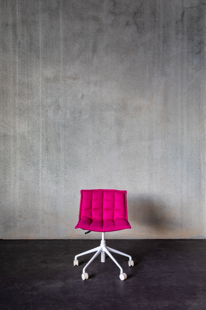 Bright pink upholstered office chair with white wheeled base against a textured grey concrete wall.