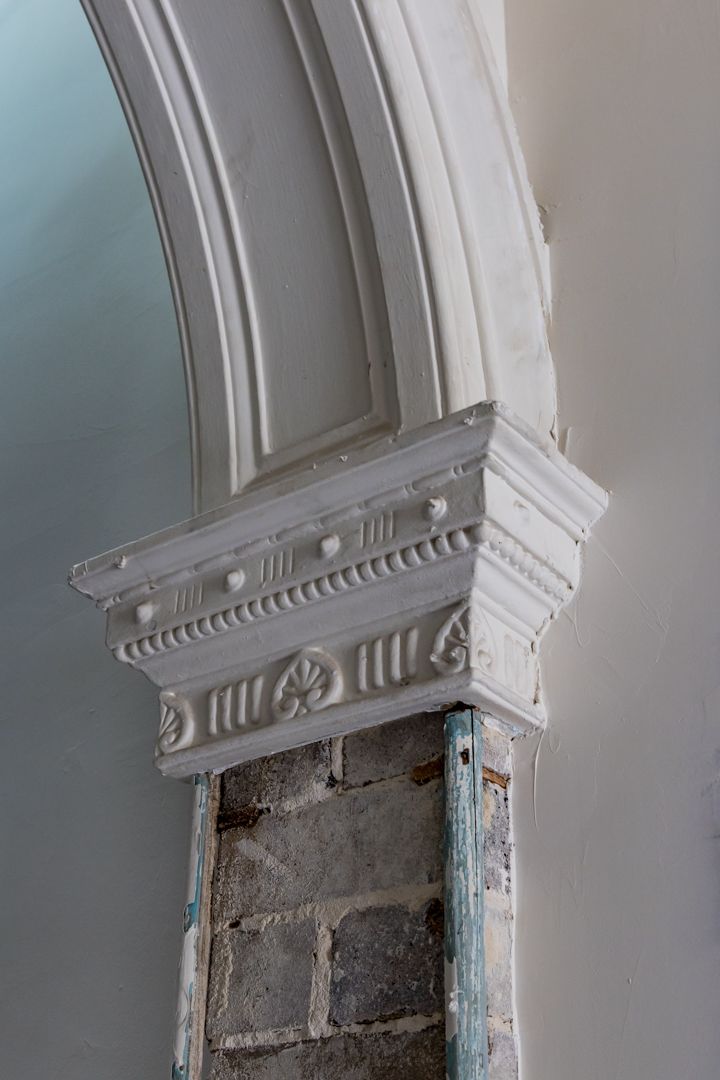 Ornate white plaster arch capital with decorative rosettes and mouldings above exposed brick during heritage building restoration.