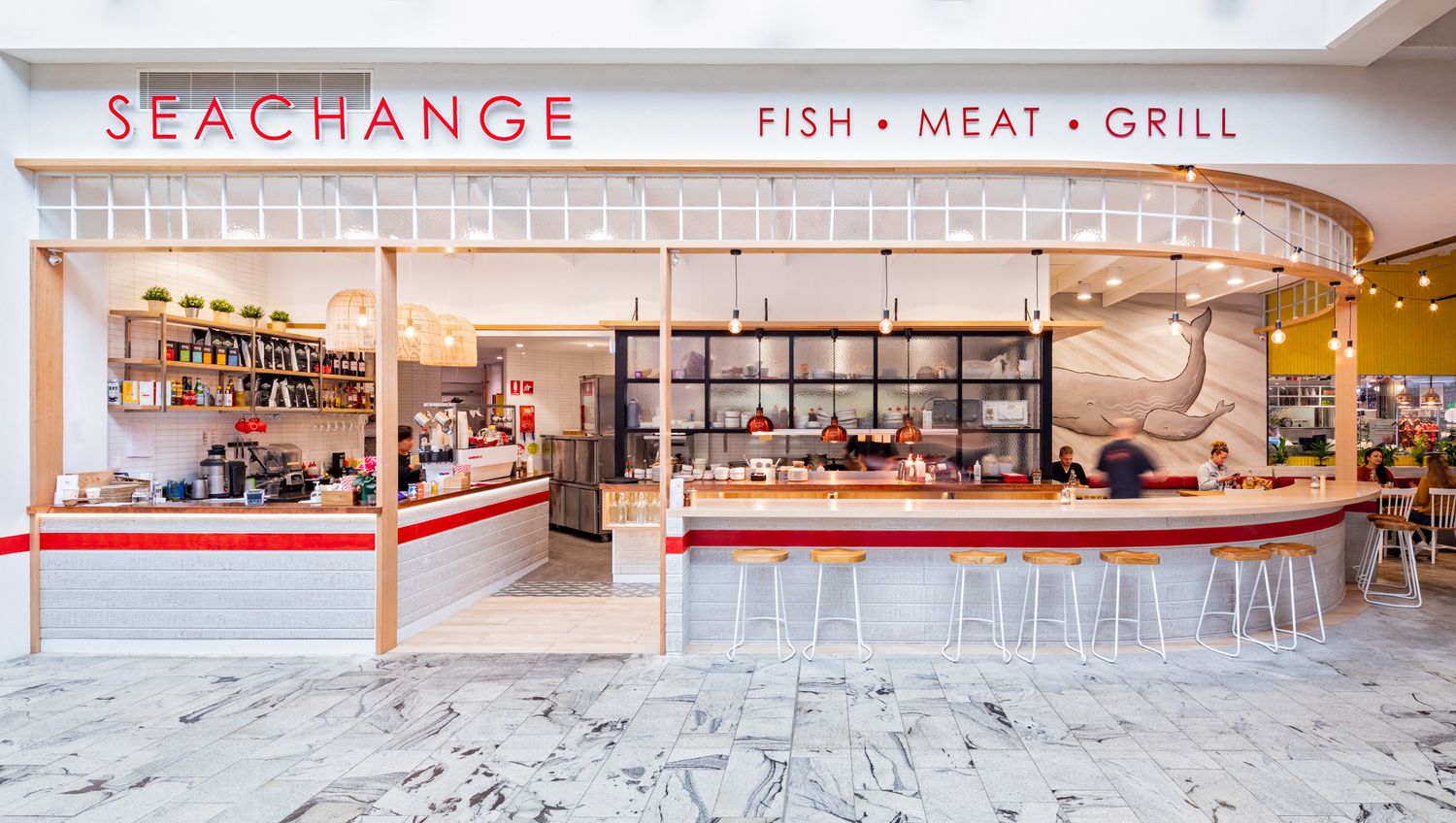 Seachange fish, meat and grill restaurant counter with pink and white striped trim, bar stools and open kitchen in a mall.