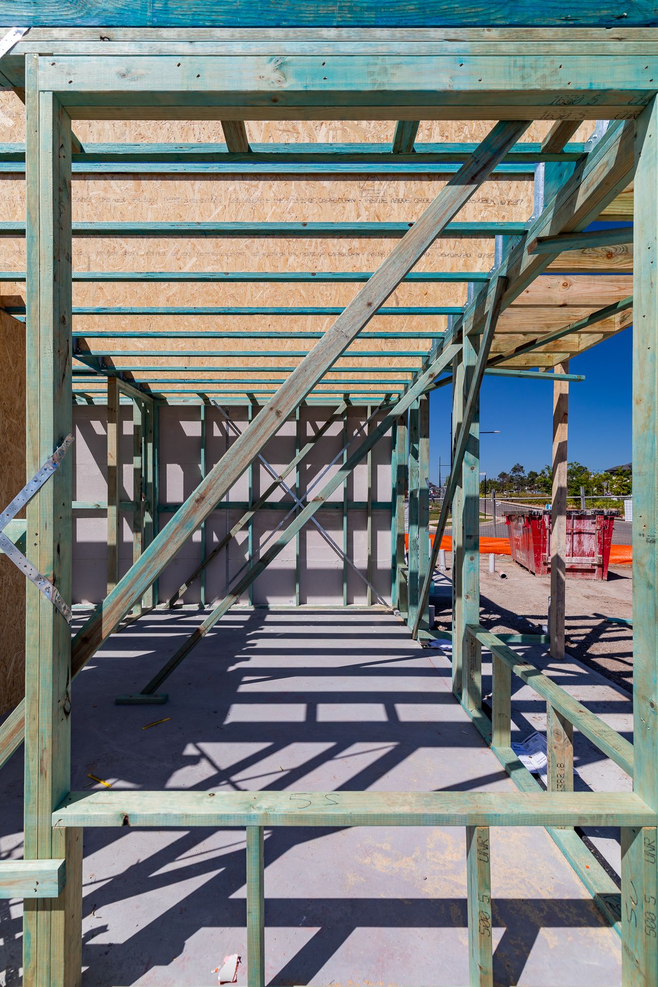 Close view of timber frame and floor joists of a multi-storey townhouse under construction, casting shadows on a concrete slab.