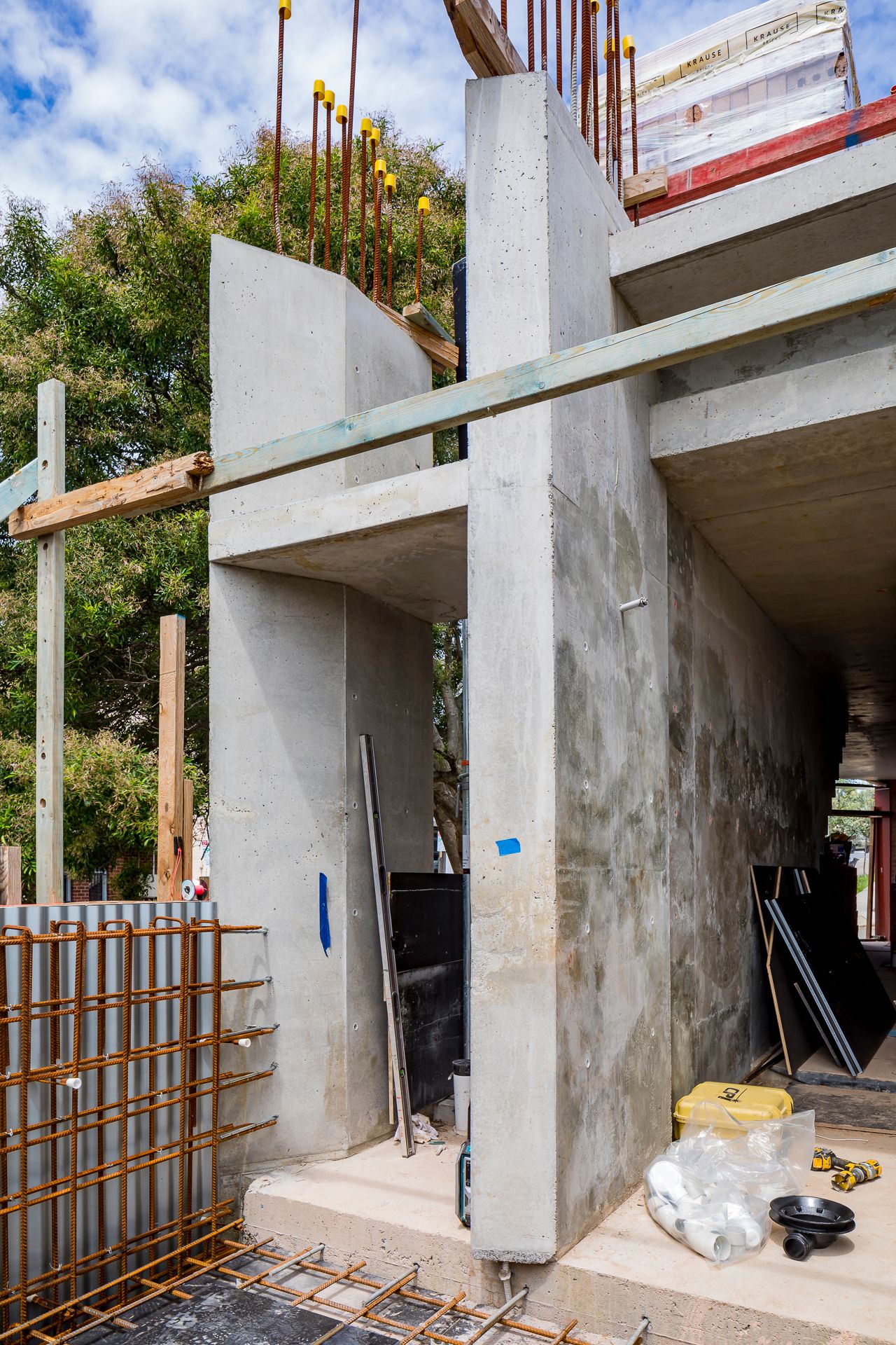 Freshly poured concrete walls and stair landing at a building site, with reinforcement bars, scaffolding and construction materials.