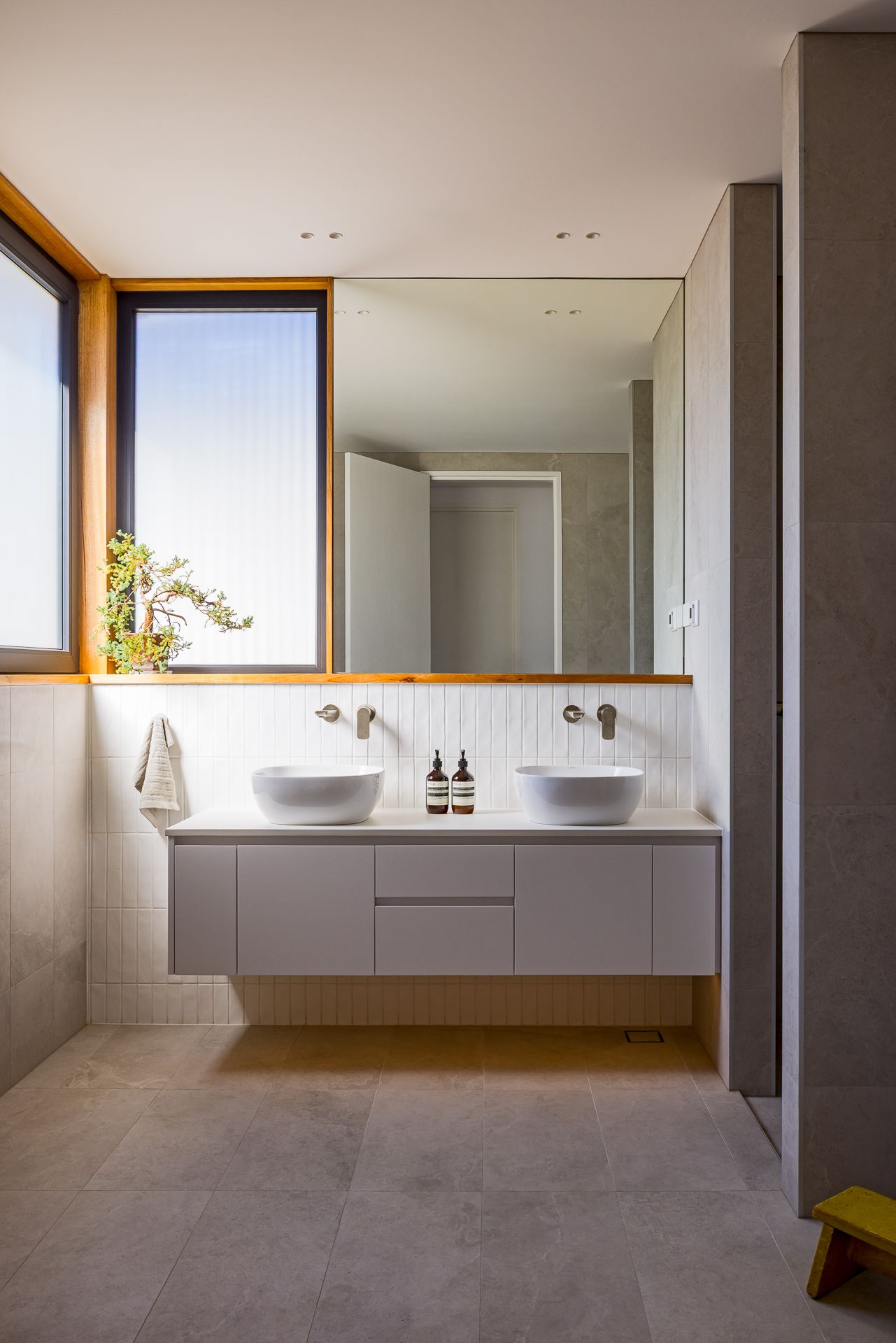 Minimalist bathroom with floating vanity, twin white vessel basins, wall-mounted taps, large mirror and timber-framed window.