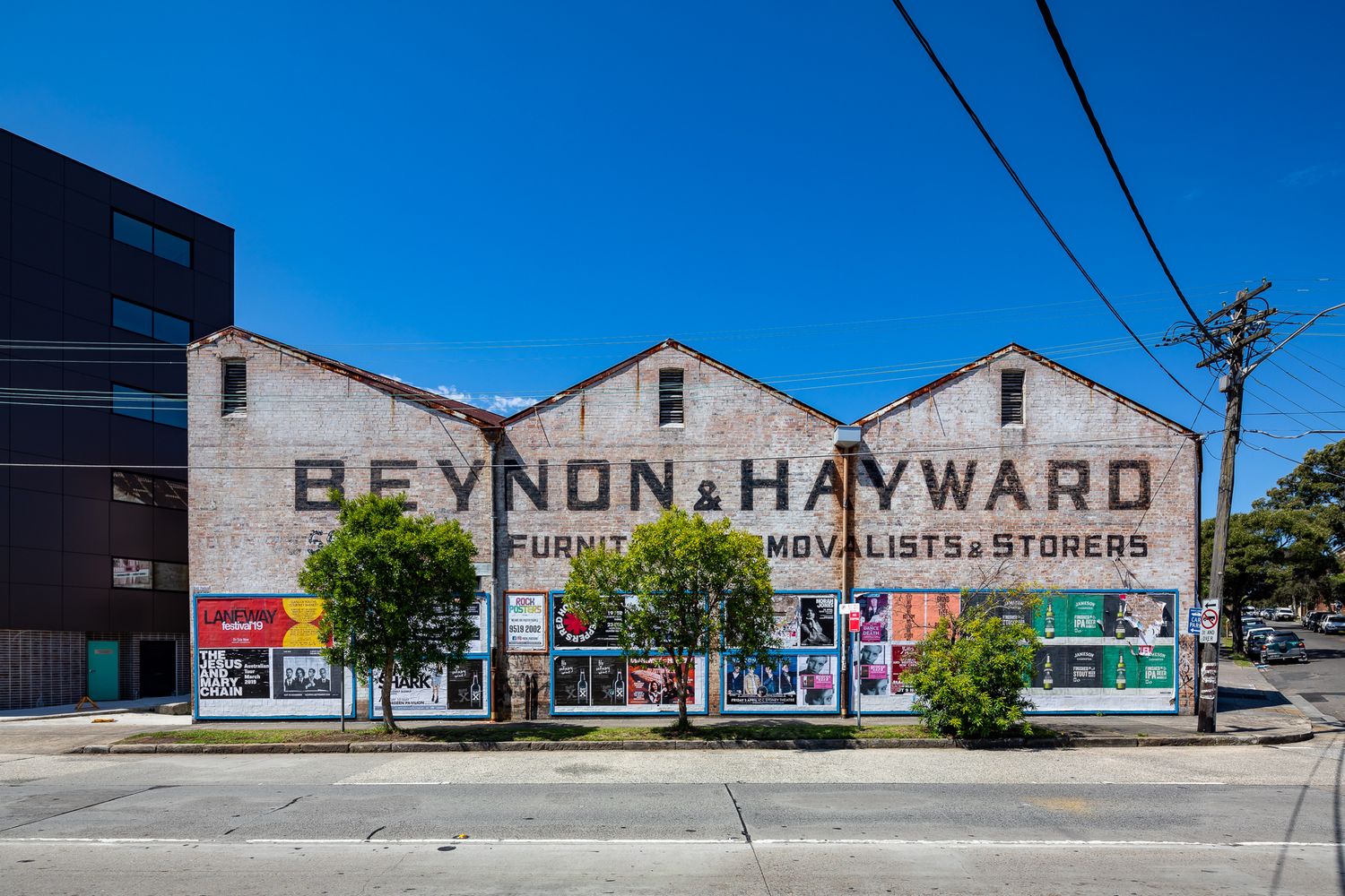 Heritage brick warehouse with a faded painted sign reading Beynon and Hayward, furniture removalists and storers, under a bright blue sky.