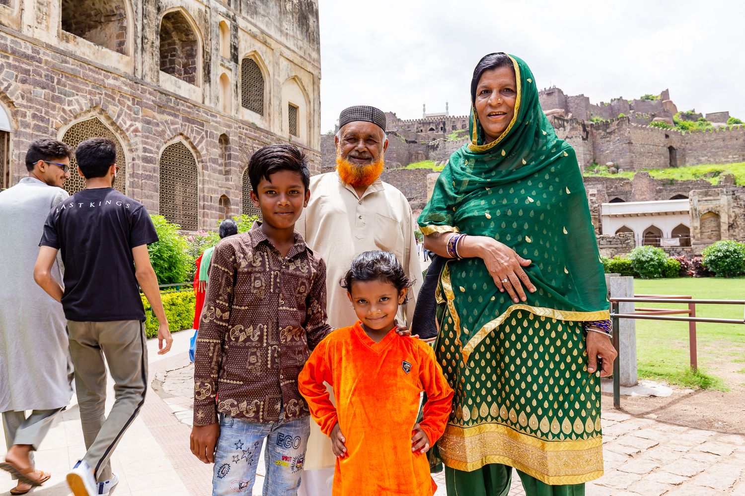 Smiling family with two children poses in front of a historic stone fort, with the woman wearing a green and gold outfit.