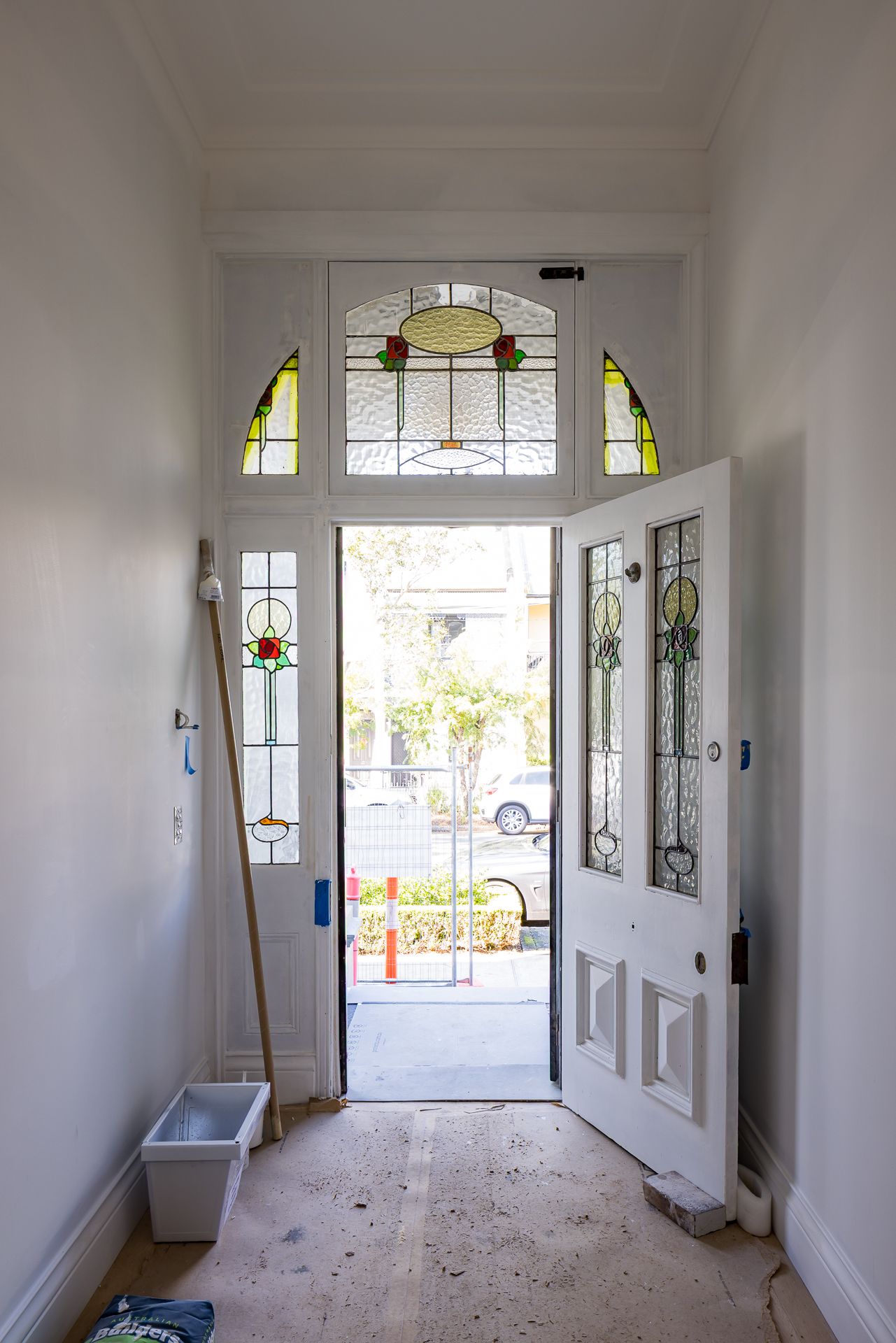 Renovated entry hall with an open front door, leadlight stained glass panels and painting supplies on a protected floor.