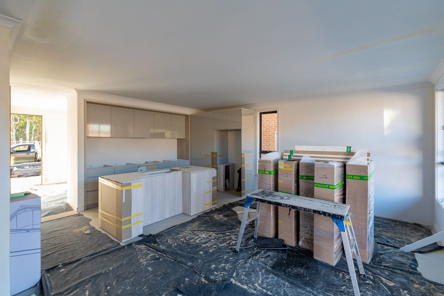 Interior of an unfinished home with new kitchen cabinets, wrapped materials and protective floor covering ready for fit-out.