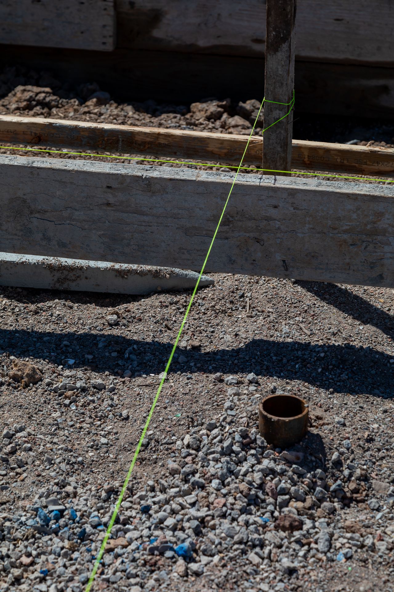 A green string line runs along timber formwork above a gravel bed with a pipe fitting at a house construction site.