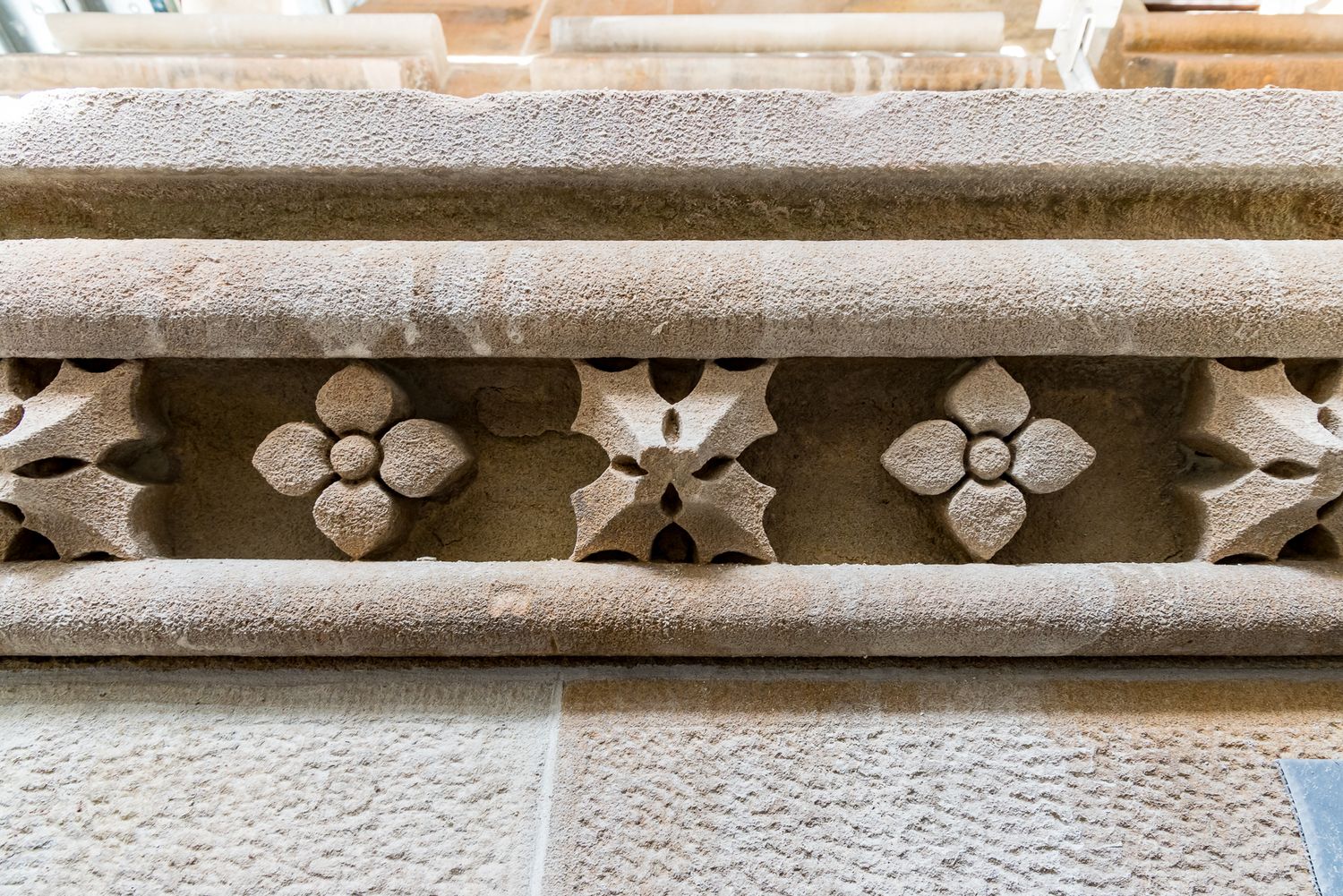 Carved stone frieze with repeating flower rosettes set between smooth horizontal moldings on a sandstone wall.