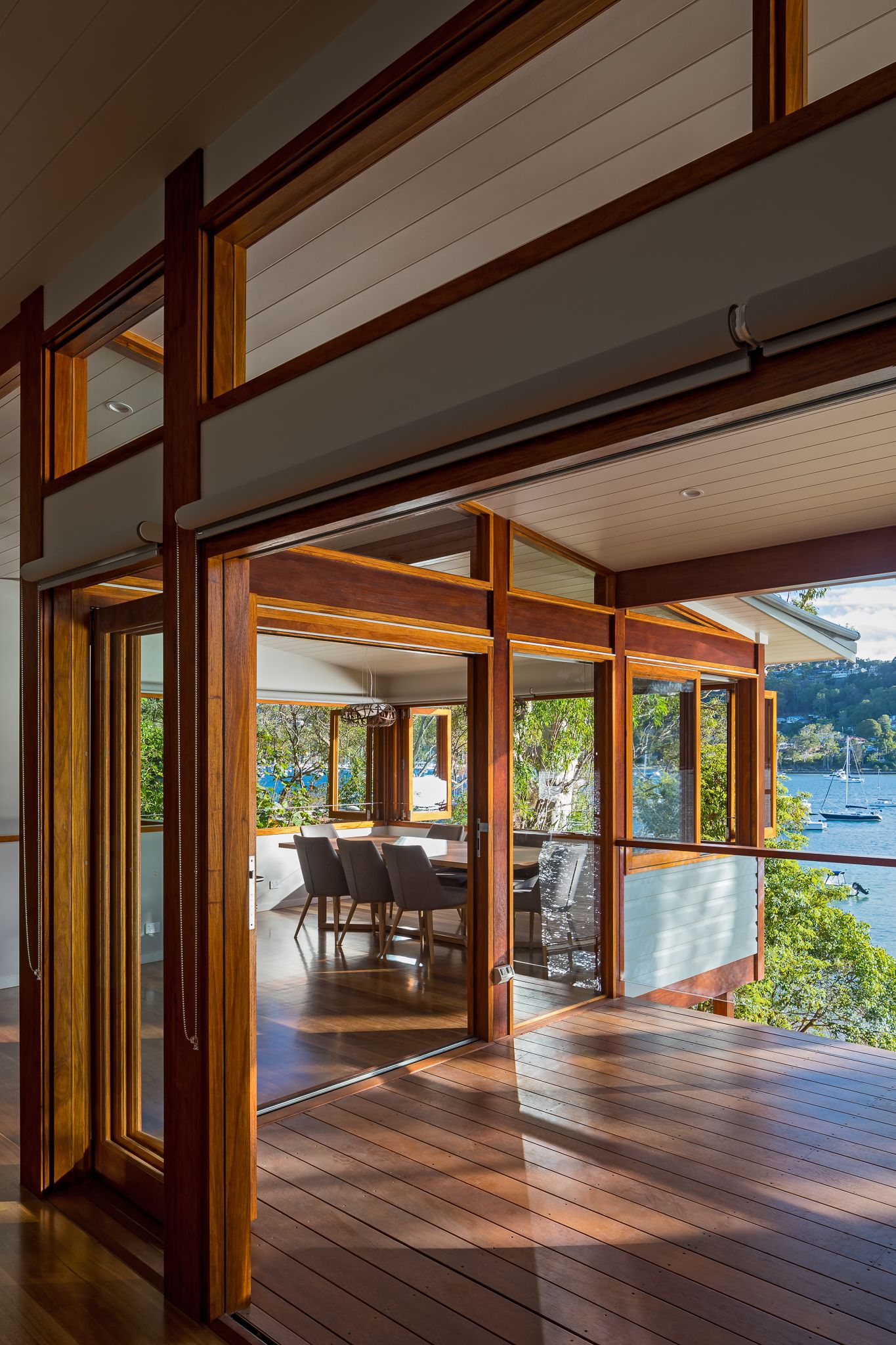 Timber-framed open-plan living area with sliding glass doors opening to a wooden deck overlooking a calm harbour.