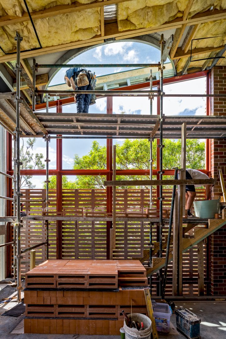 Construction workers on scaffolding inside a brick building with a large arched window and insulation overhead.