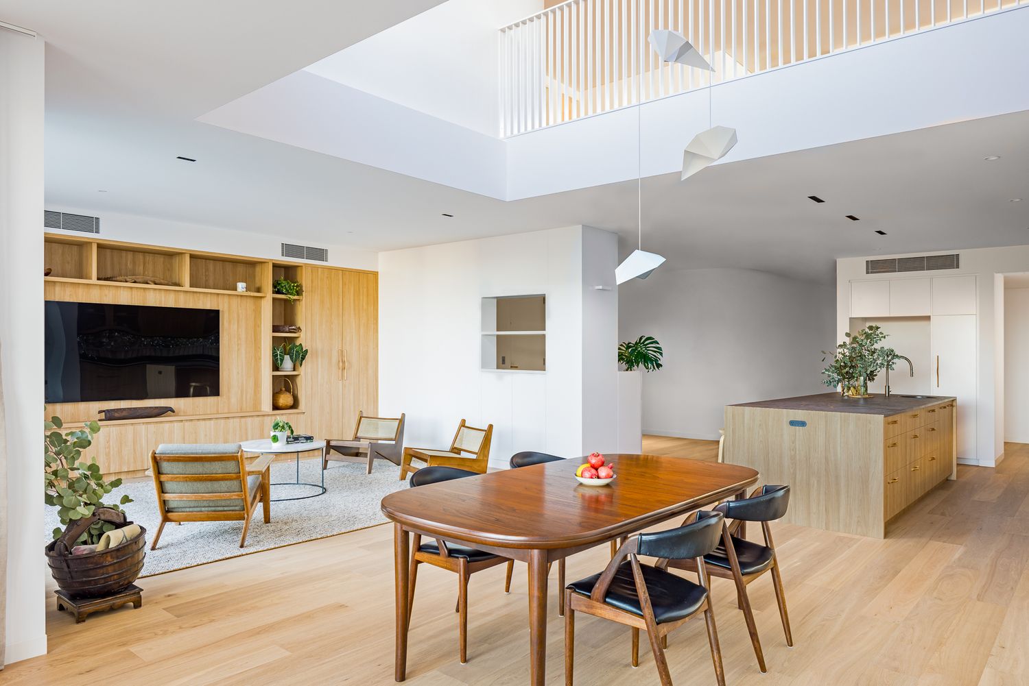 Open-plan living and dining area with timber dining table, oak floors, built-in media unit, kitchen island and mezzanine above.