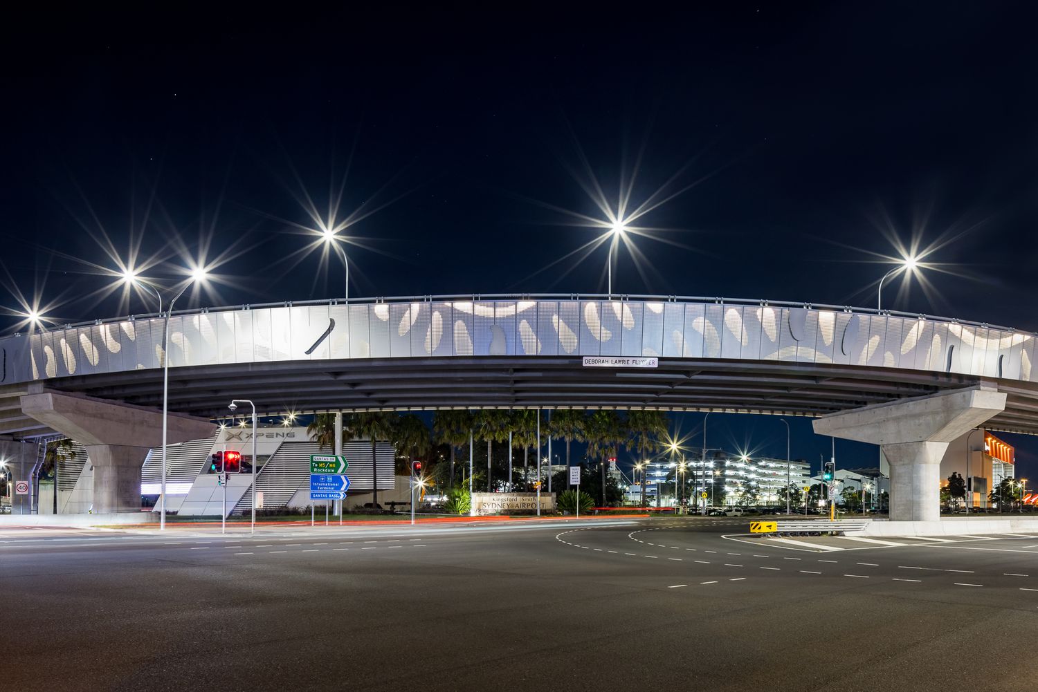 Wide view of a curved overpass with a decorative leaf-patterned facade over an intersection at night.
