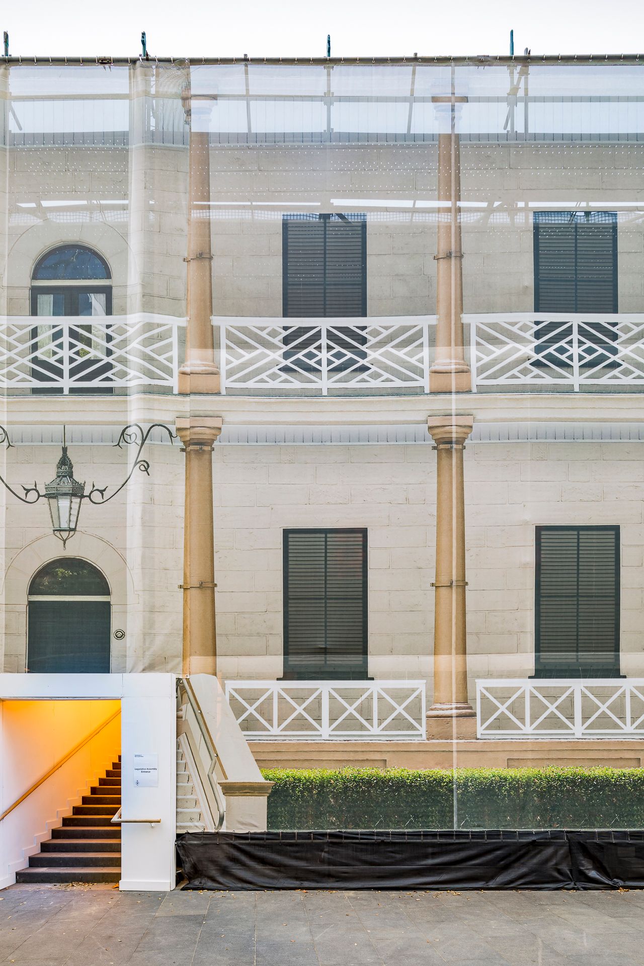 Historic colonial-style building facade with white balustrade balconies, tall columns and dark shutters, viewed through a translucent screen