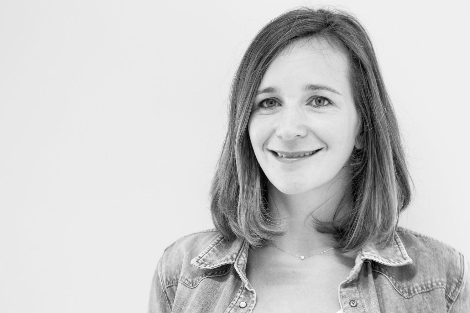 A black and white portrait of a smiling woman with shoulder-length hair wearing a denim jacket against a plain white background.