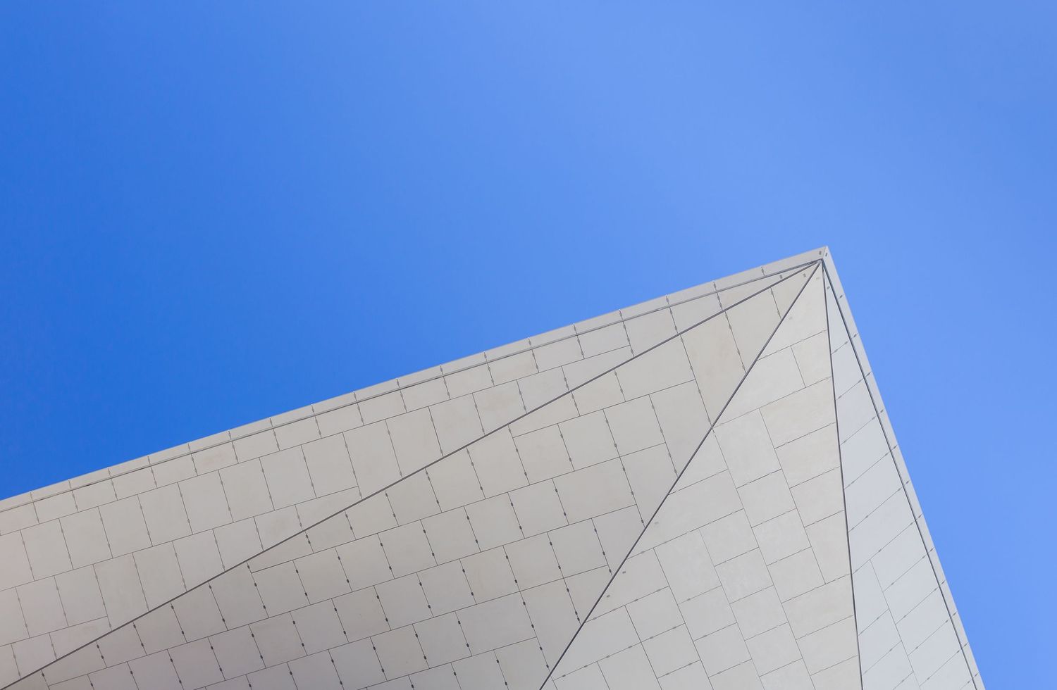 Abstract low-angle view of a white tiled angular roof edge against a deep blue sky.