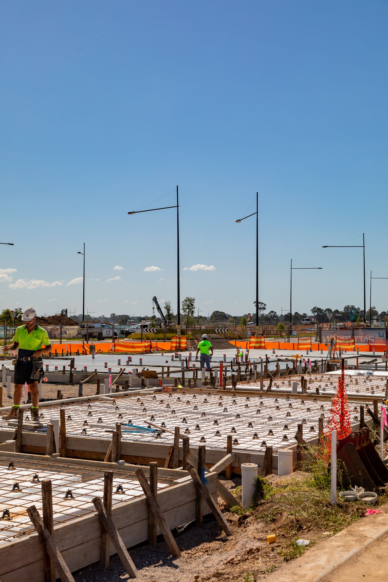 Workers in hi-vis clothing standing on timber formwork around steel reinforcement for concrete slabs at a housing development.