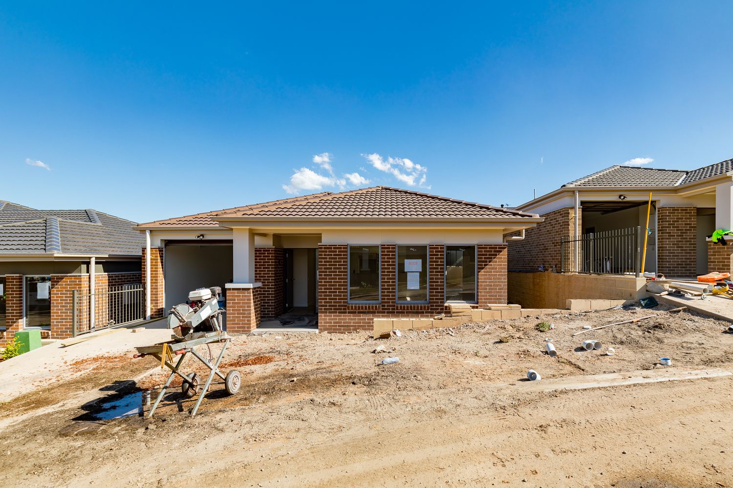 Brick home under construction with a tiled roof, unfinished front yard and a cement mixer on a dirt building site.