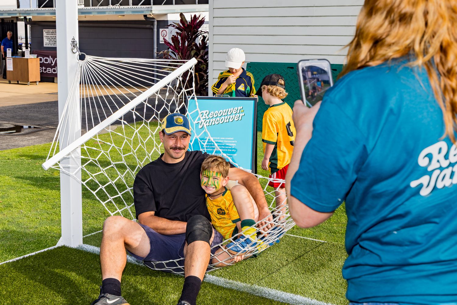 Father and child relax together in a soccer goal net hammock at a family-friendly football fan event.