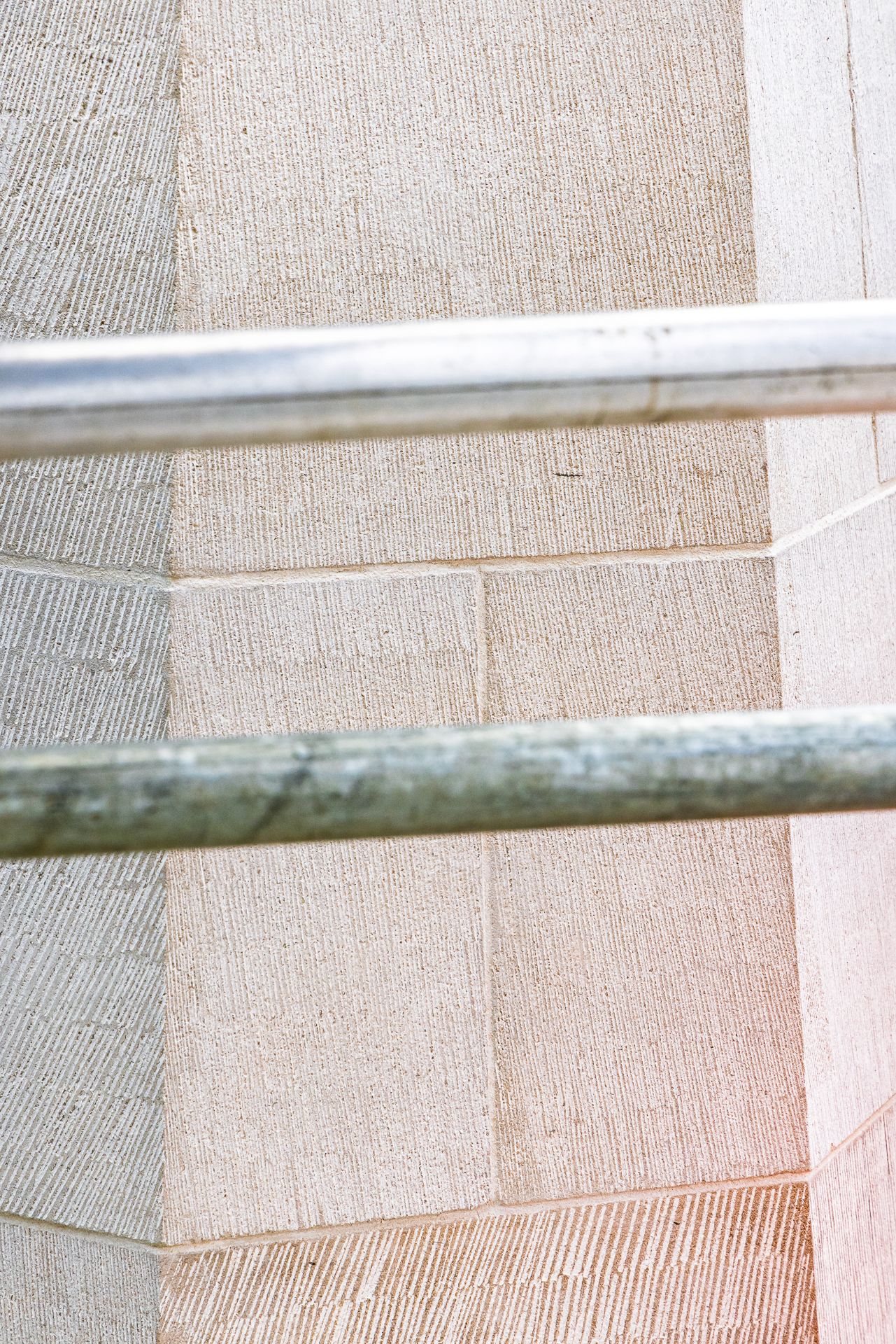 Close-up of textured sandstone blocks with fine tooled finish seen behind two horizontal metal scaffolding tubes.