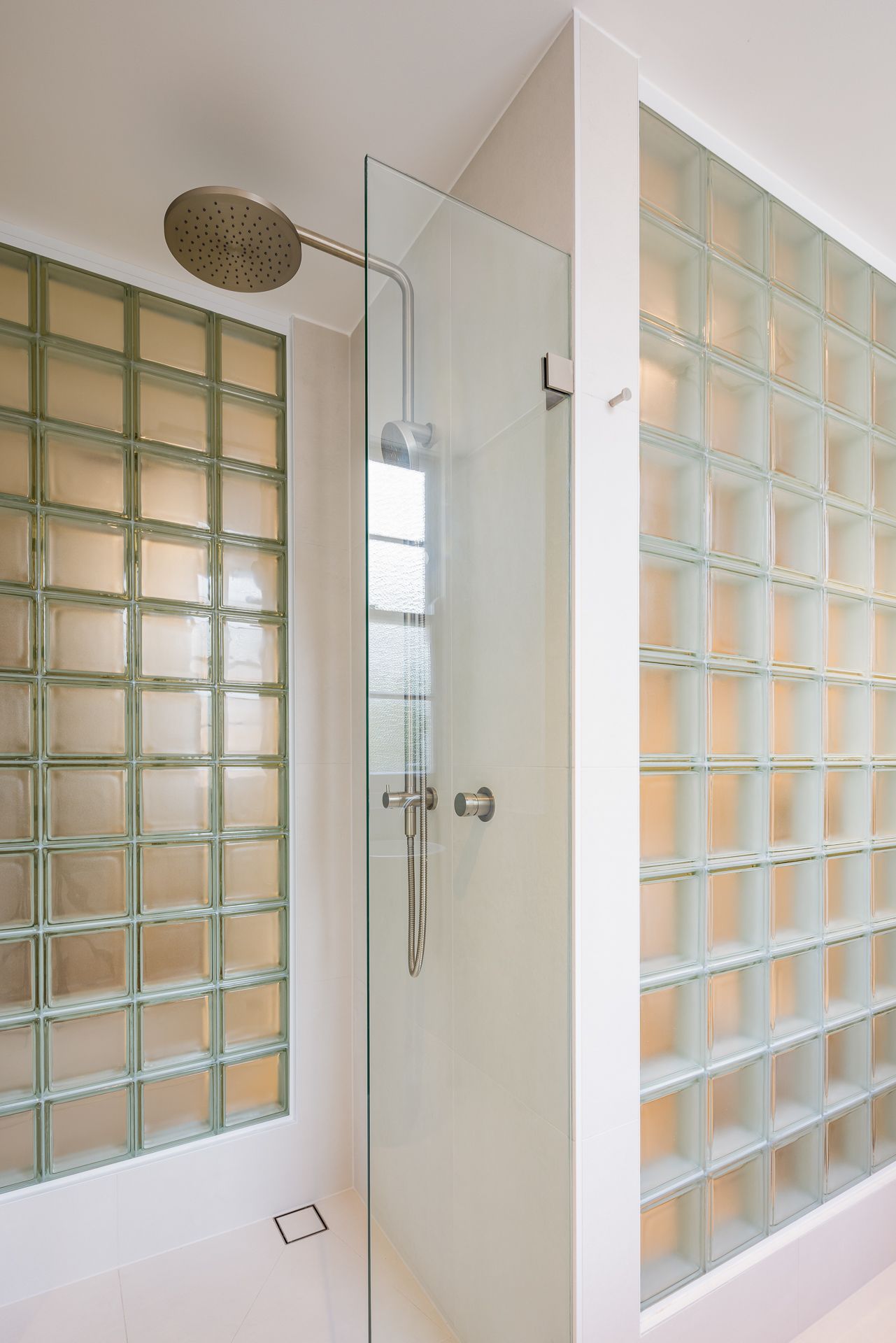 Modern walk-in shower with a round rain showerhead, frameless glass panel and glowing glass block walls.