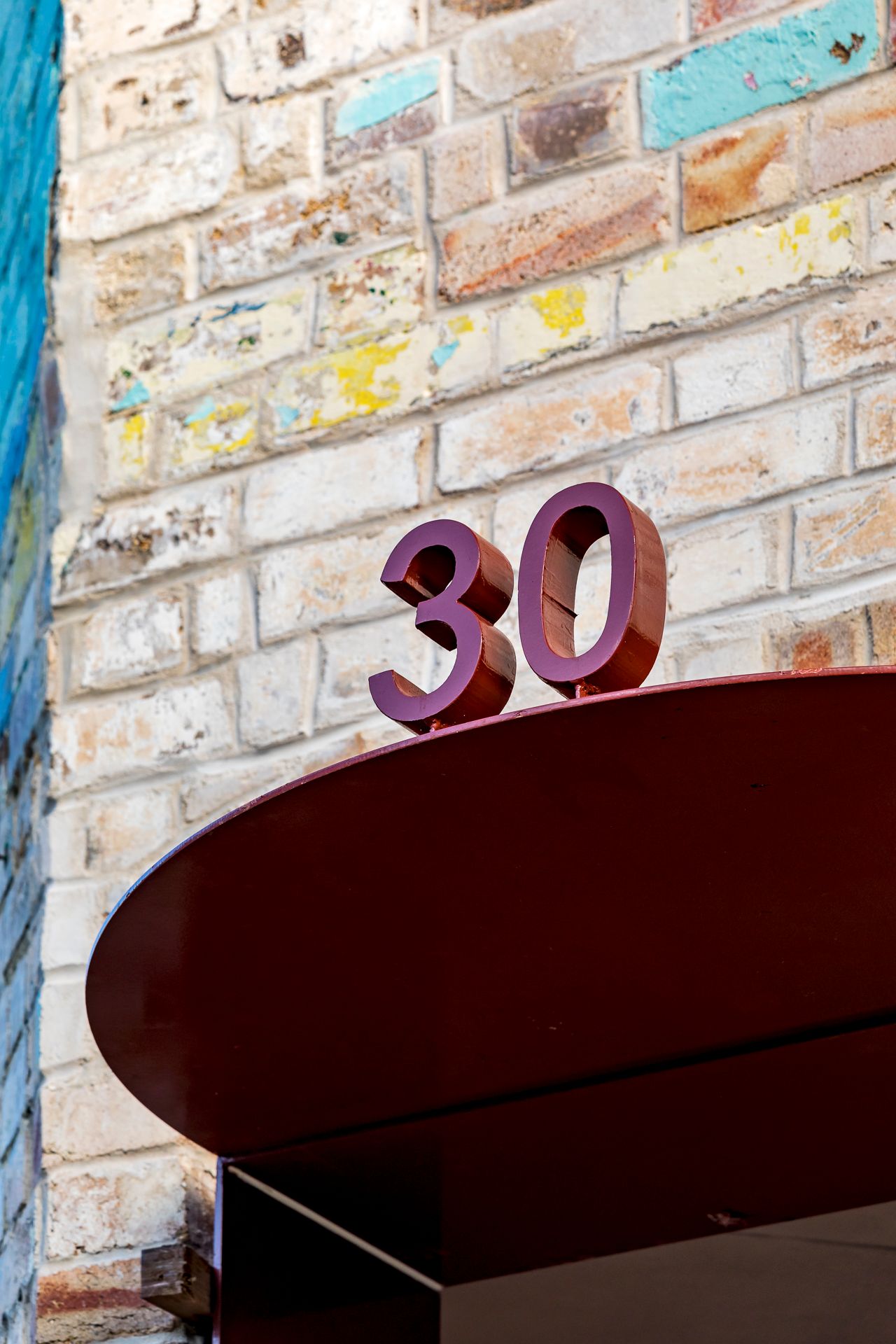 Red number 30 sign on a curved canopy against a colorful painted brick wall with blue and yellow patches.