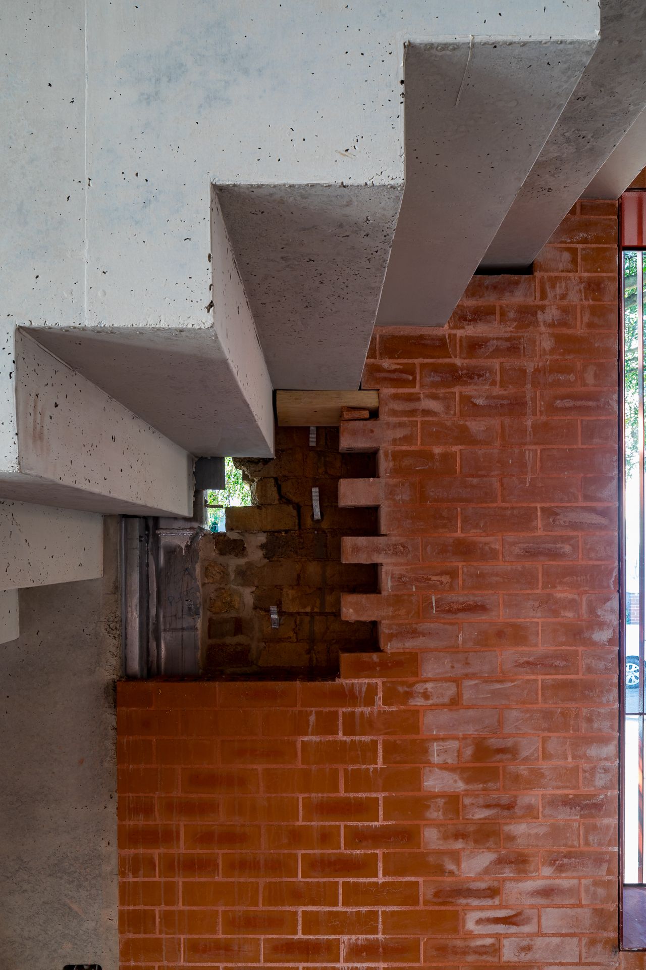 Floating concrete stair treads built into a red brick wall, showing raw architectural material contrast.