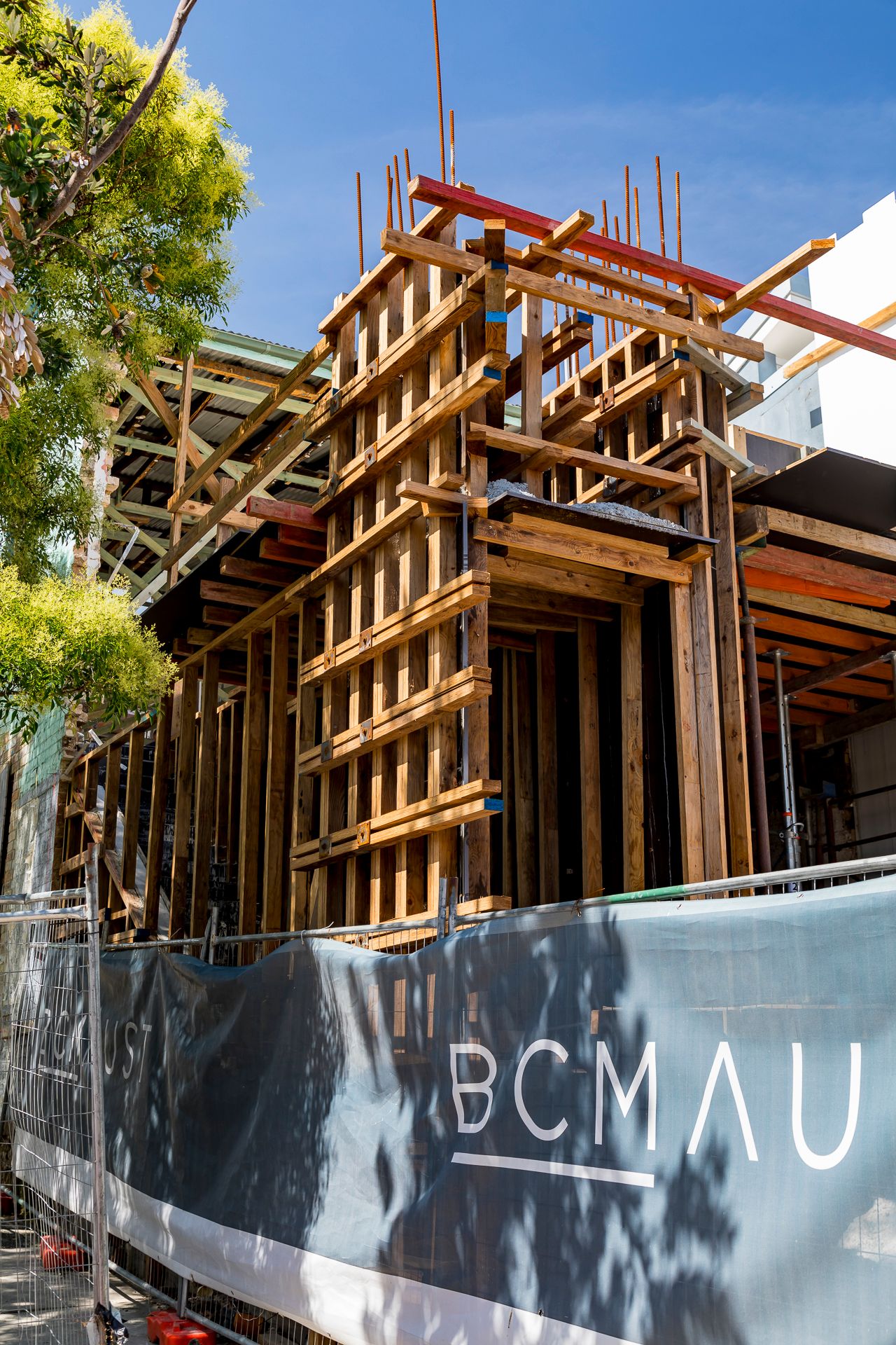 Timber formwork and propping for a multi-level building under construction, with a BCMAU branded site hoarding in the foreground.