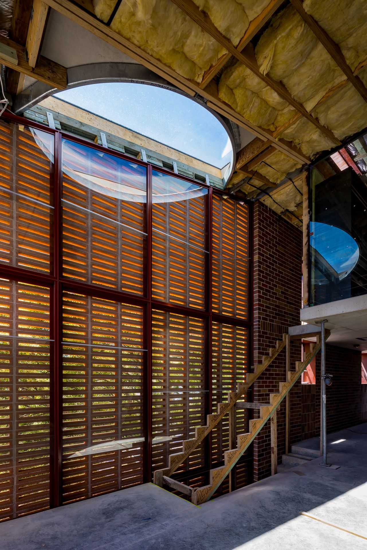 Brick building under construction with a large round skylight, timber louvre screens and a steel staircase.