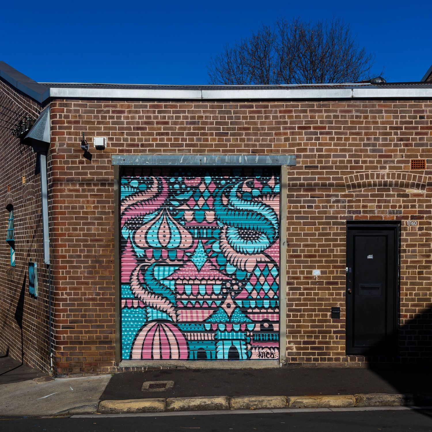 Colorful pink, teal and blue street art mural with ornate domes painted on a roller door of a brick building.