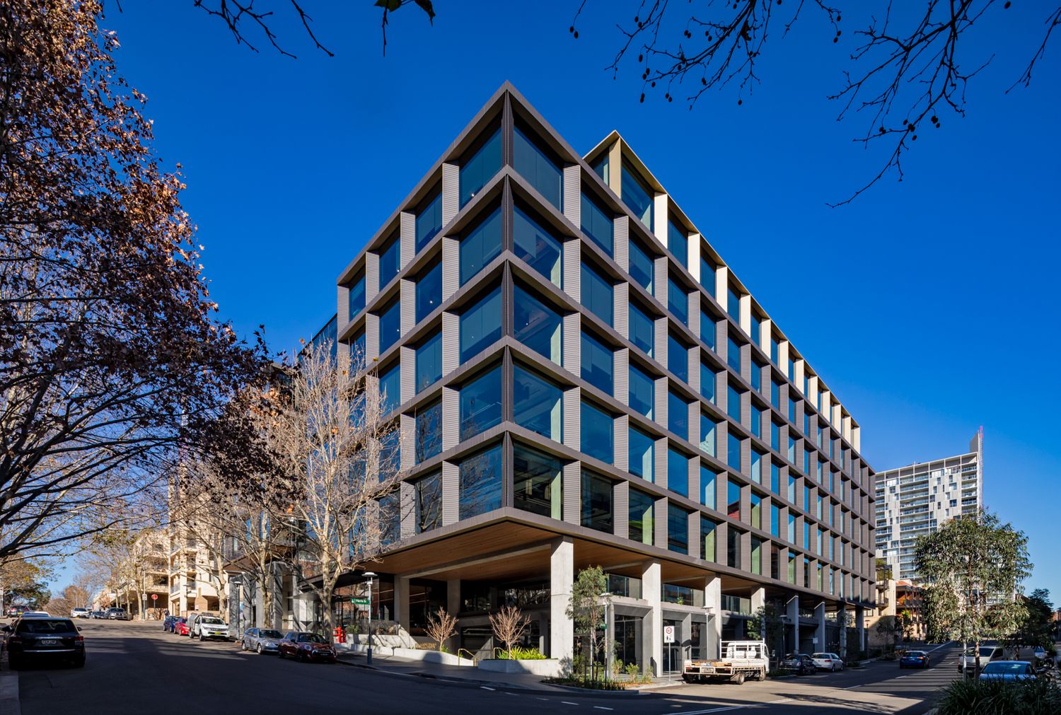 Contemporary multi-level office building with a gridded glass facade on a tree-lined city street.