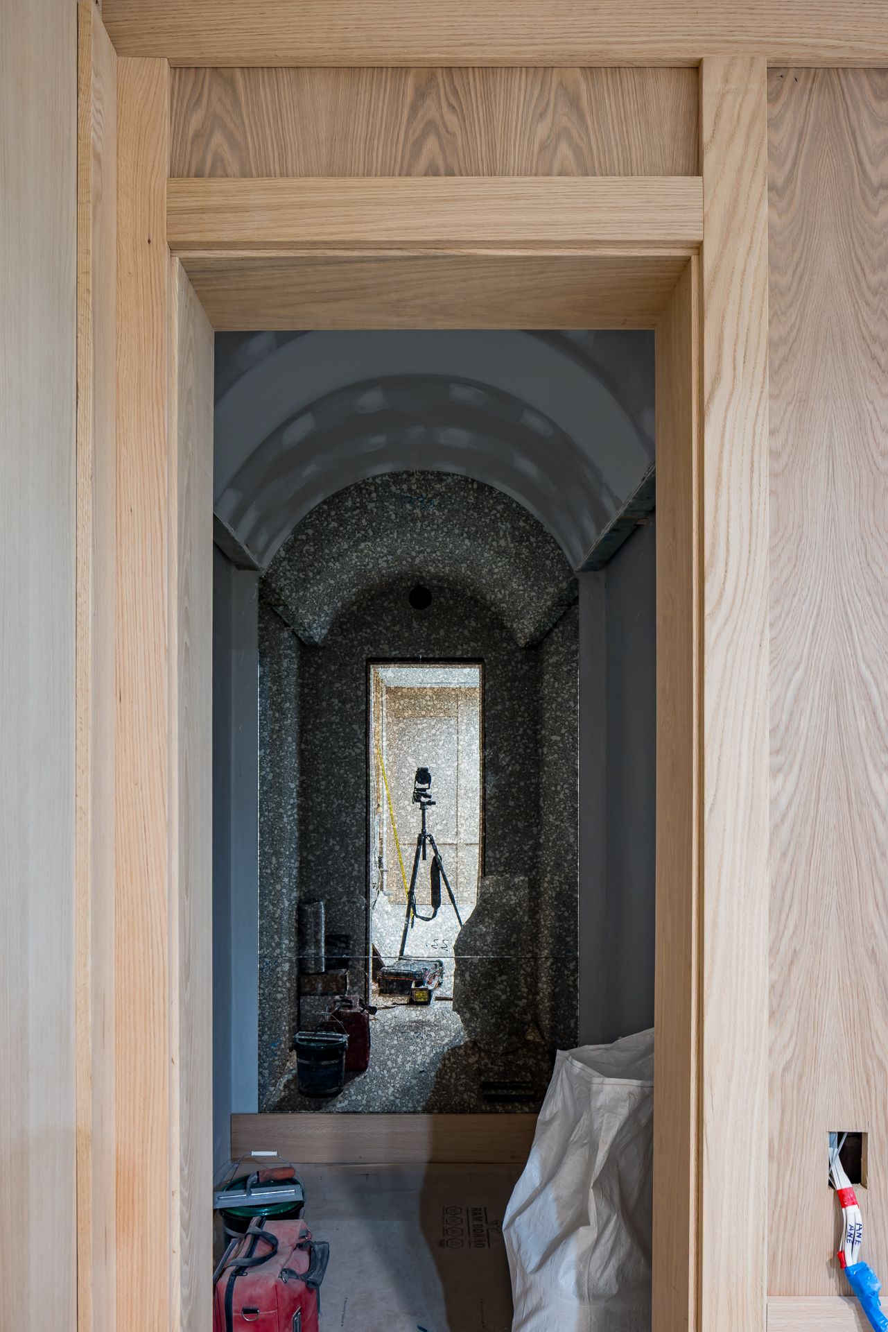 View through an oak-framed doorway to a vaulted hallway with speckled stone-effect walls, a camera tripod and building equipment.