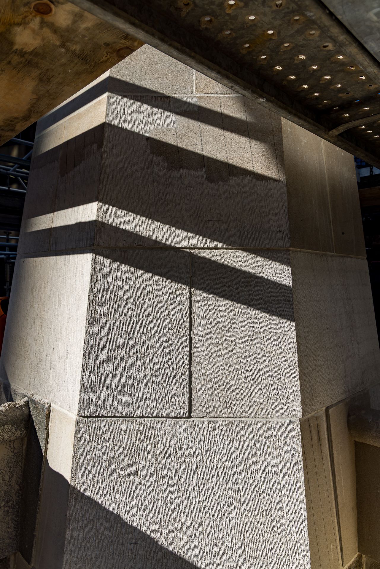Large tapered limestone pier with angled blocks and dramatic diagonal shadows beneath a ceiling with recessed lights.