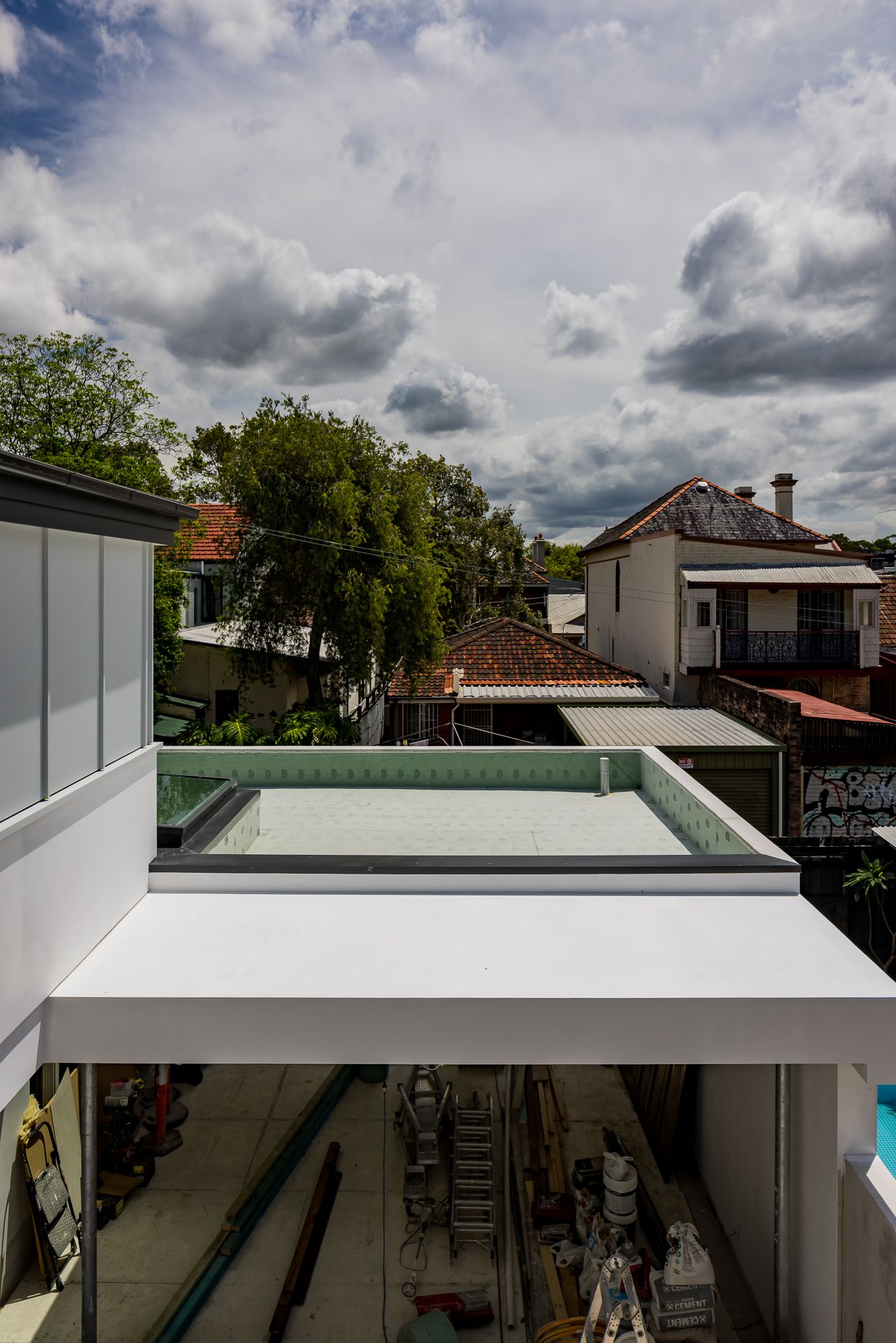 View over a skylight and rooftops of surrounding houses and trees beneath a cloudy sky, with a construction area below.