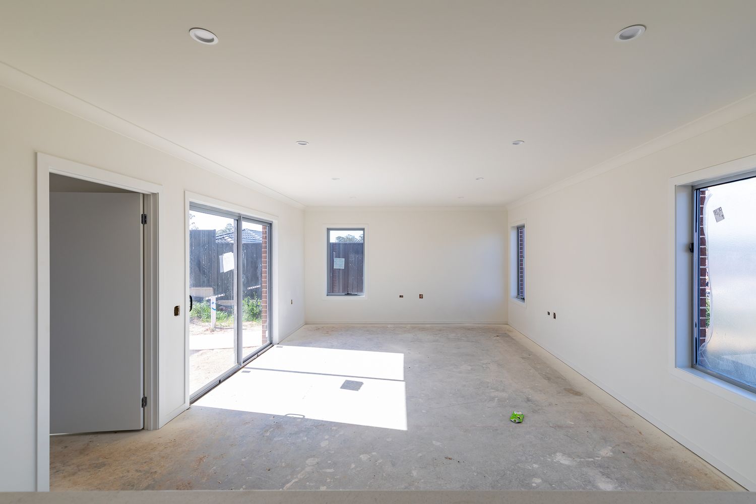 Bright unfinished living room with bare concrete floor, sliding glass door, and window ready for final fit-out in a new home.