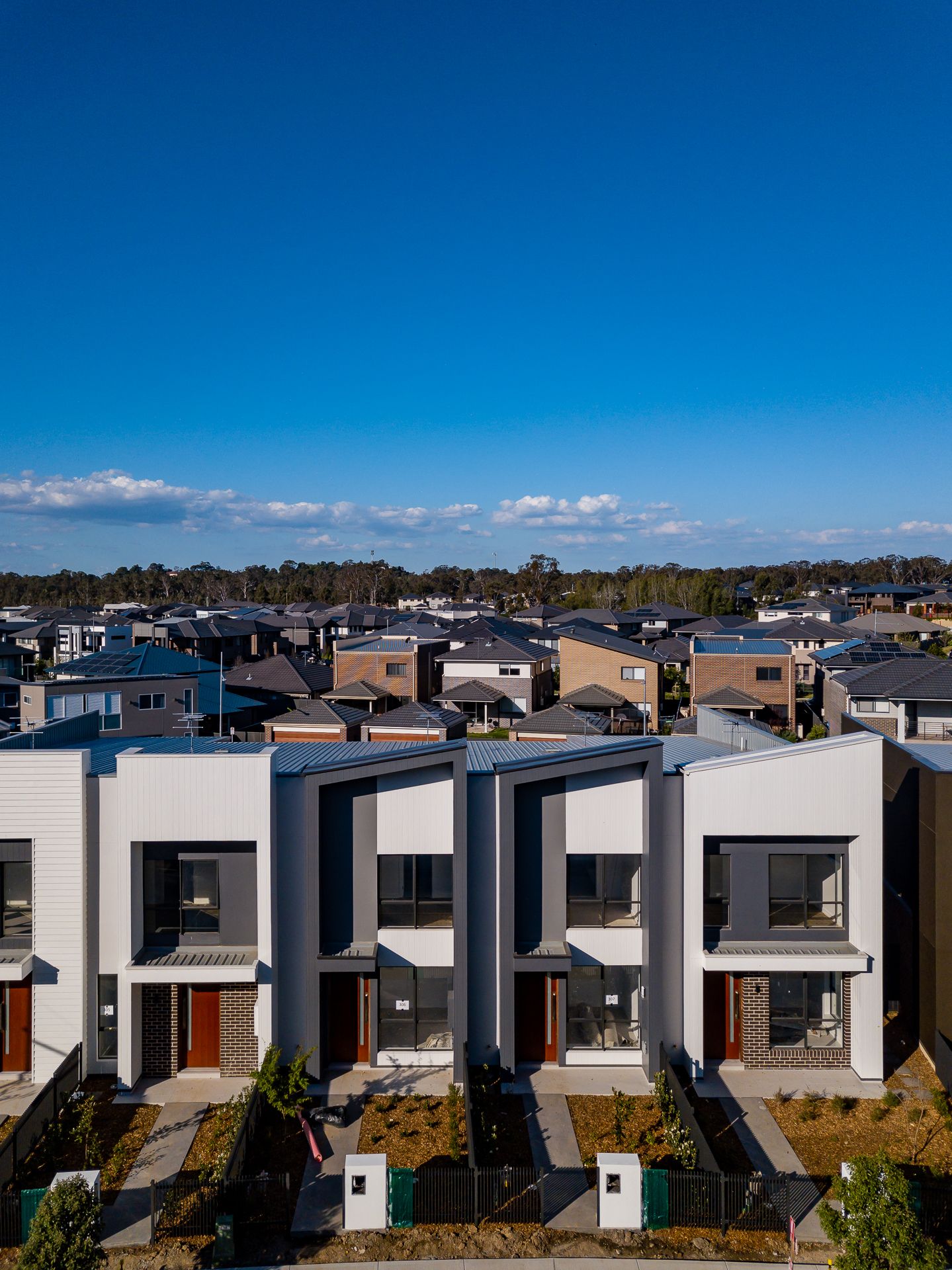 Row of modern two-storey townhouses with white and grey facades and red doors beneath a clear blue sky.
