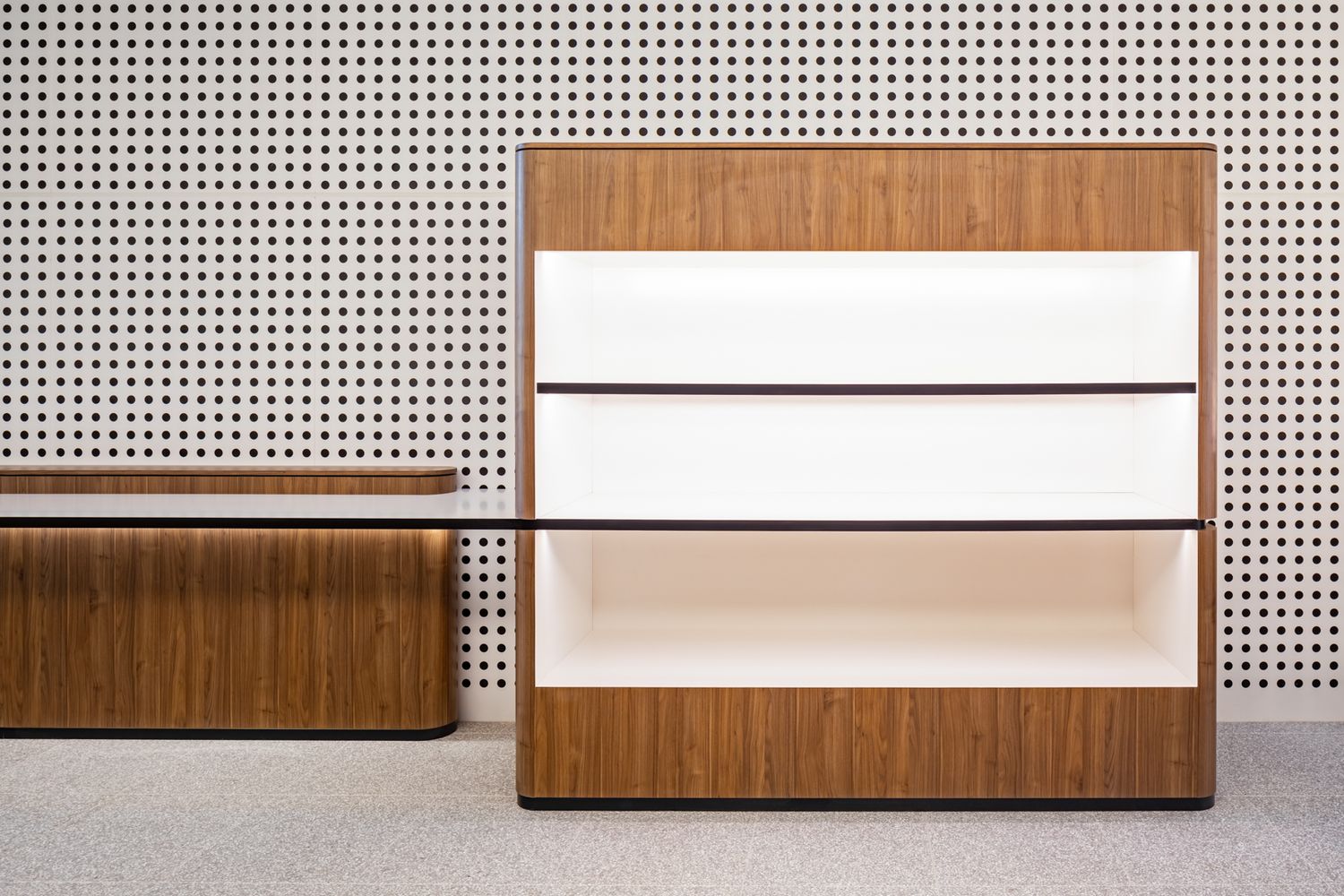 Walnut timber shelving unit with backlit white shelves against a wall of perforated acoustic panels.