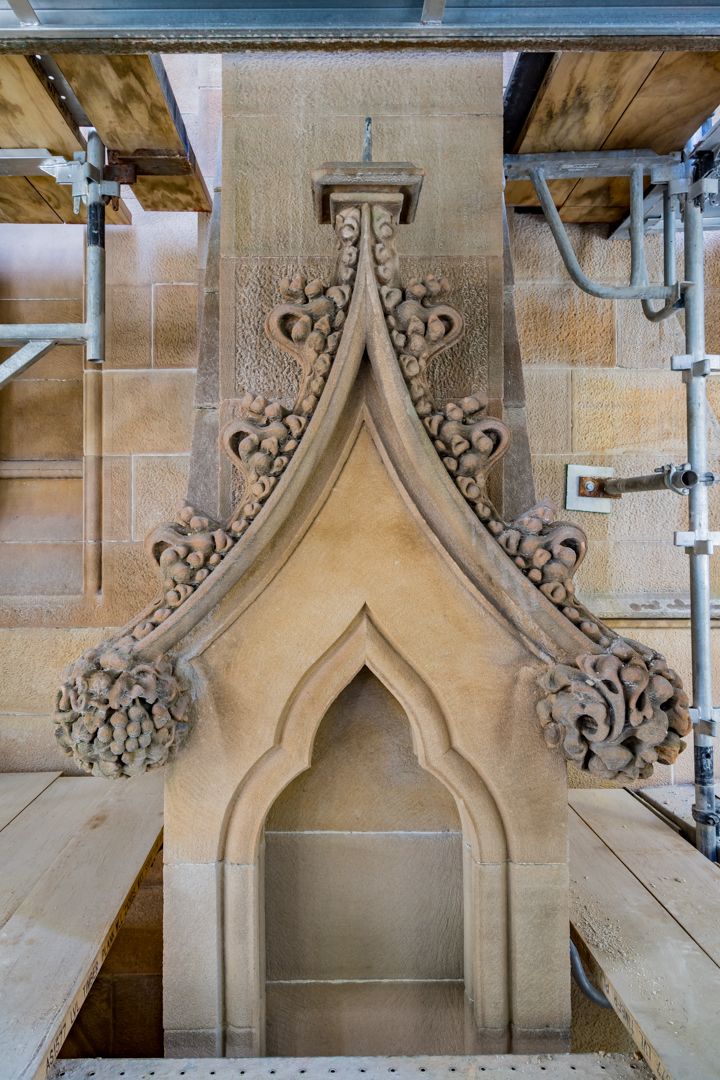 Ornate carved sandstone Gothic niche with decorative crockets, surrounded by scaffolding and timber planks during heritage restoration.