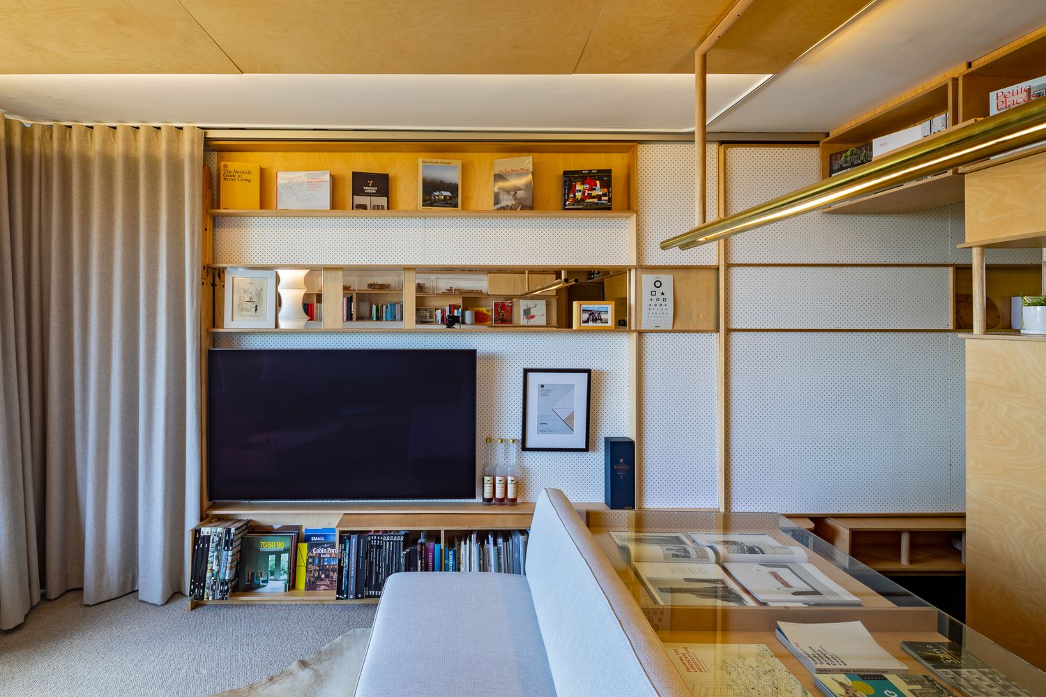 Cozy apartment living area featuring a flat-screen TV, built-in wood bookshelves and a glass-topped table.