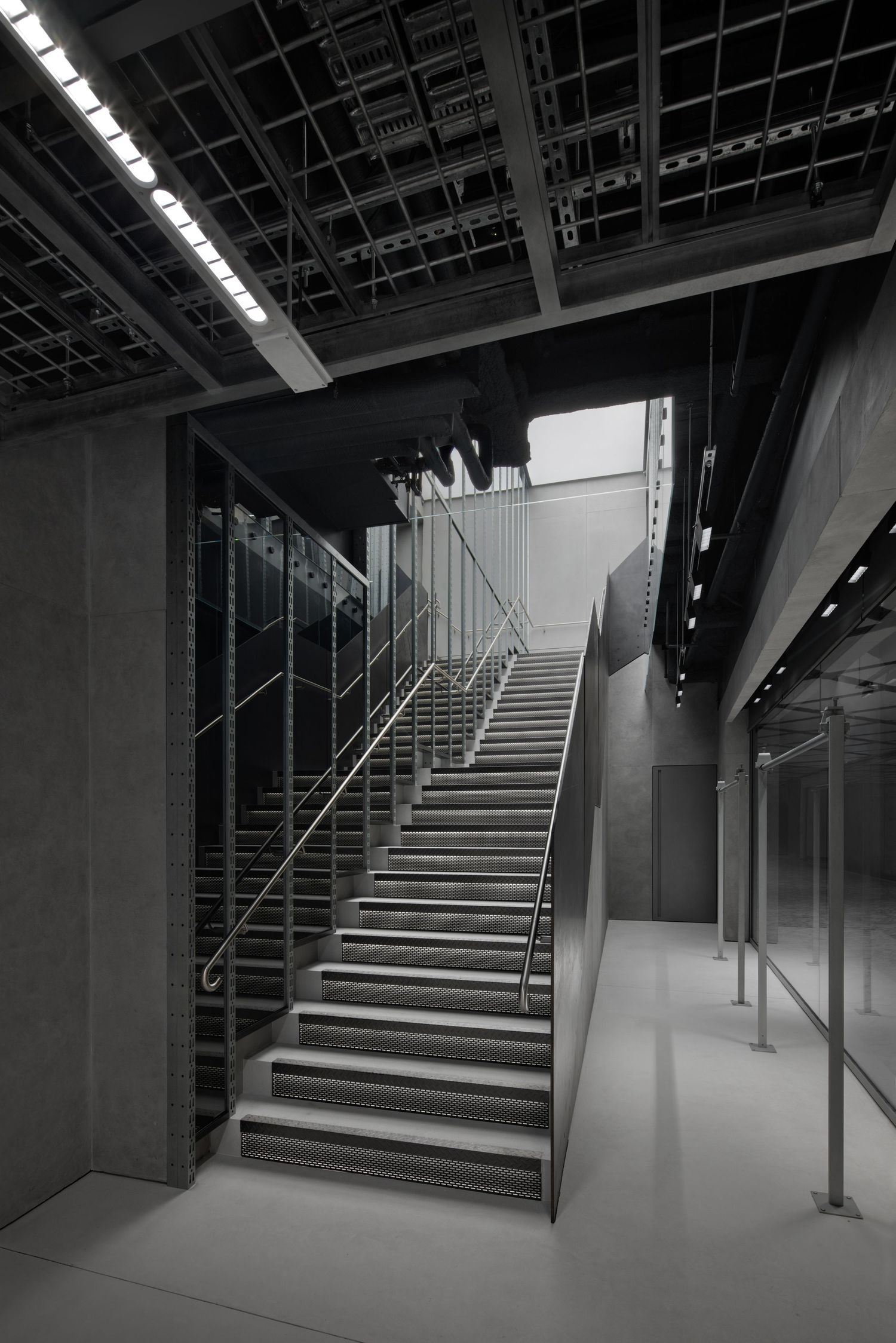 Dramatic industrial staircase with metal railings, concrete walls, exposed ceiling grid, and glass partitions inside a modern luxury store.