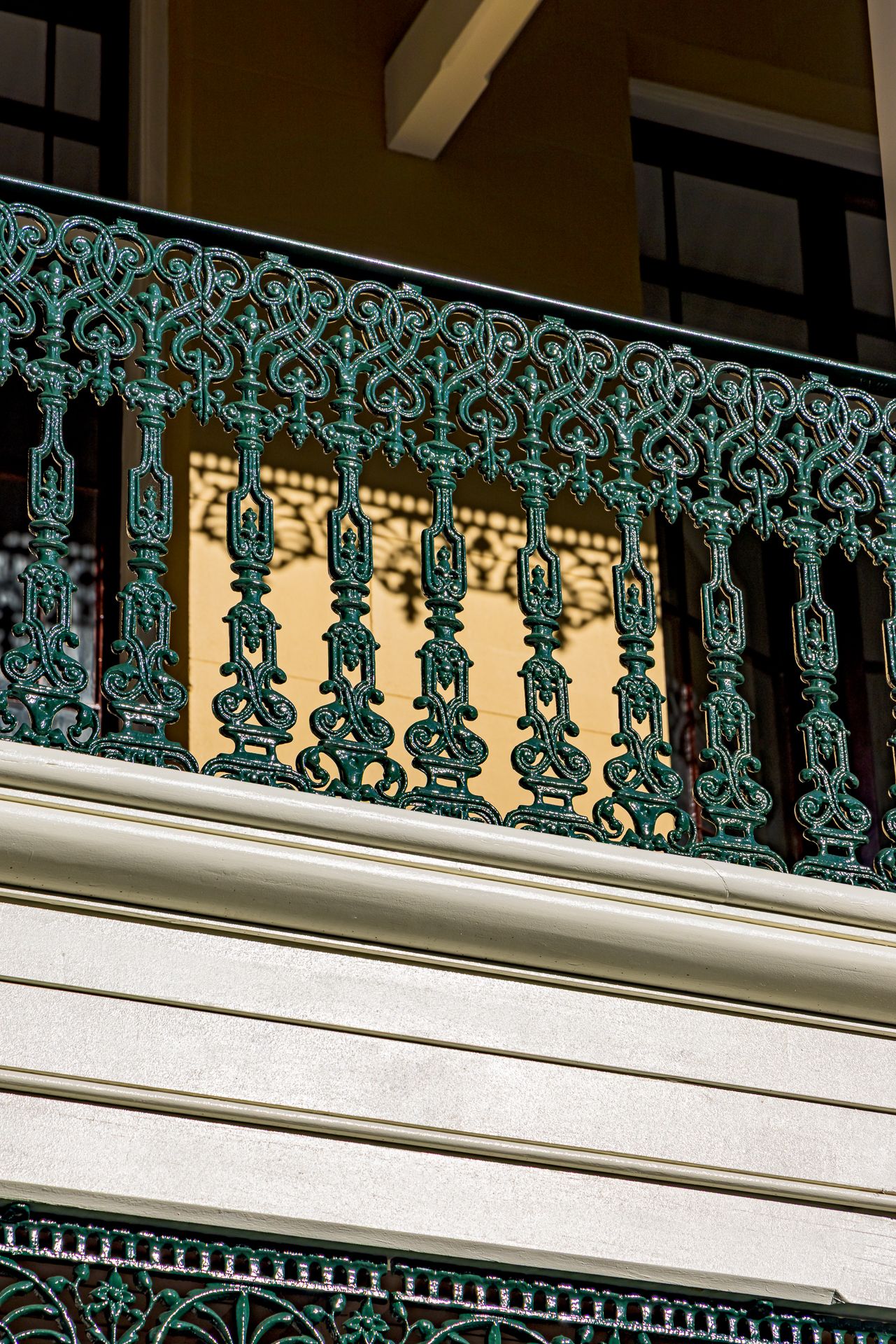 Close-up of an ornate green cast-iron balcony balustrade with intricate scrollwork on a heritage building.