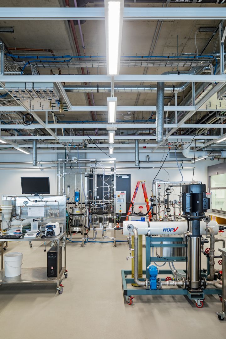 Industrial laboratory space with exposed ceiling services, pumps, piping and process equipment on a polished concrete floor.