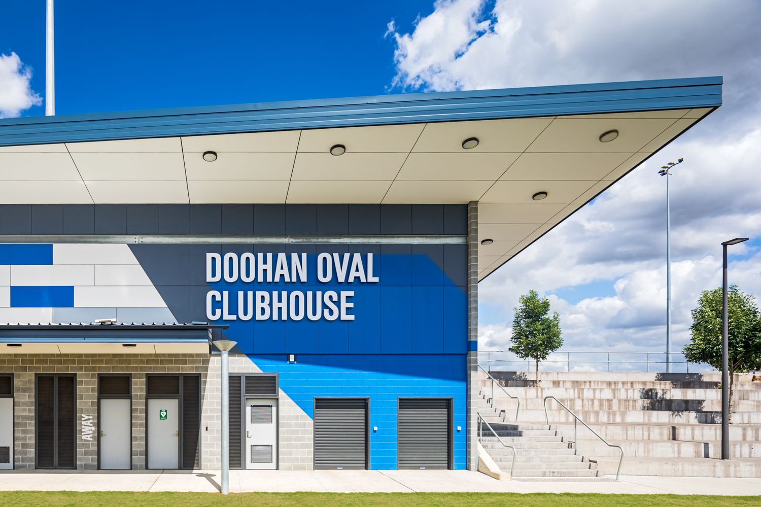 Doohan Oval Clubhouse with a blue and white facade, cantilevered roof and concrete grandstand seating beneath a partly cloudy sky.