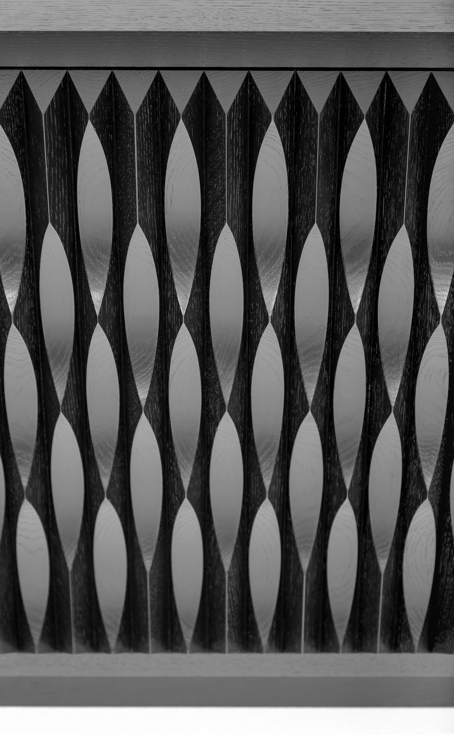 Close-up of a black wooden cabinet front with a carved, rhythmic leaf-shaped pattern over a brushed metallic background.